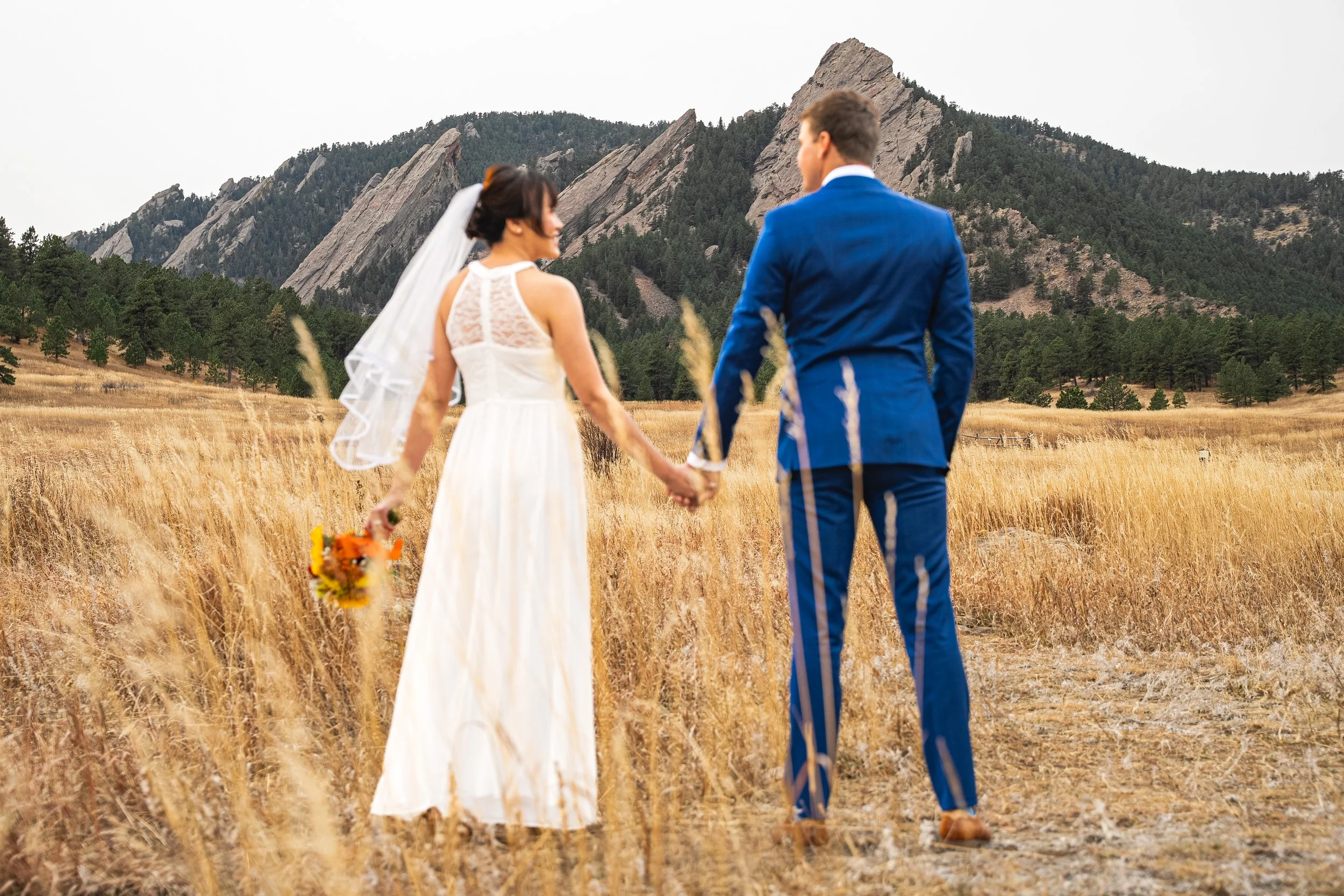 A wedding couple holding hands and looking into the distance.  They are out of focus and the mountains in the distance are intentionally focused.  Beautiful landscape photography