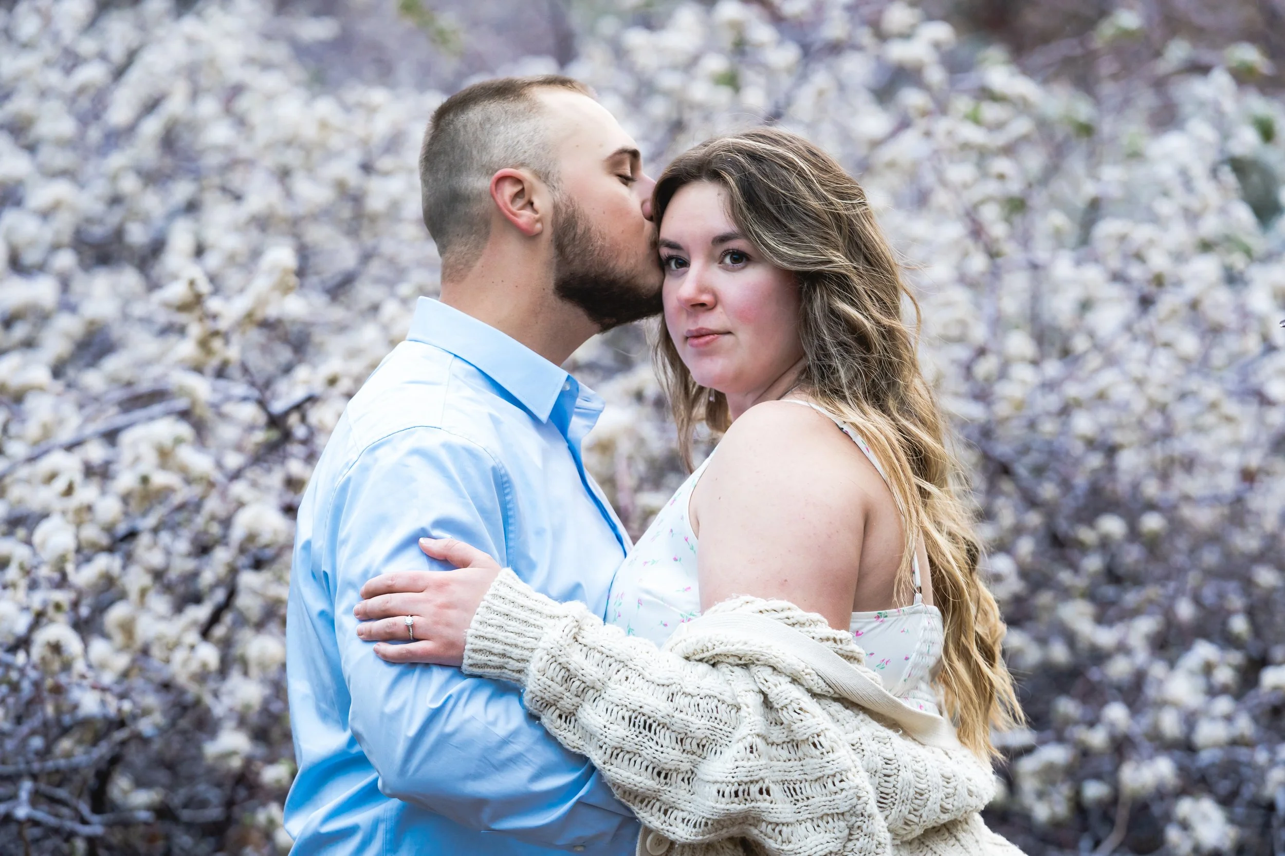 Sunrise engagement photo session.  The entire background is frozen flower buds from a snap freeze the night prior.  This photo seems editorial with the female's hand and engagement ring placed on her fiancés arm, yet naturally posing together. 
