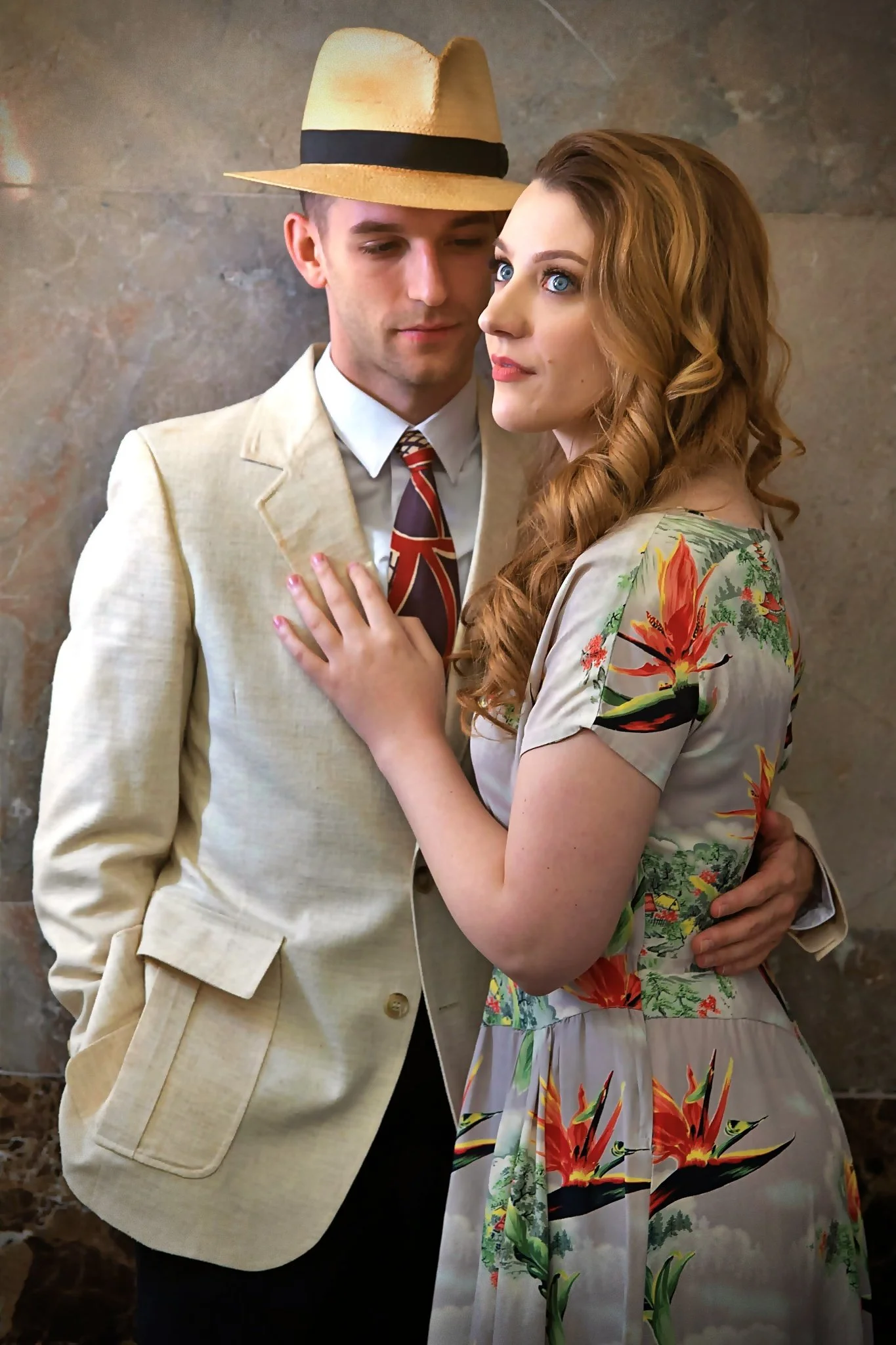 Couple’s portrait photography by An Entropy Production of a man in a beige suit and straw hat with a woman in a floral dress, standing closely and looking at each other. Family photography with An Entropy Production