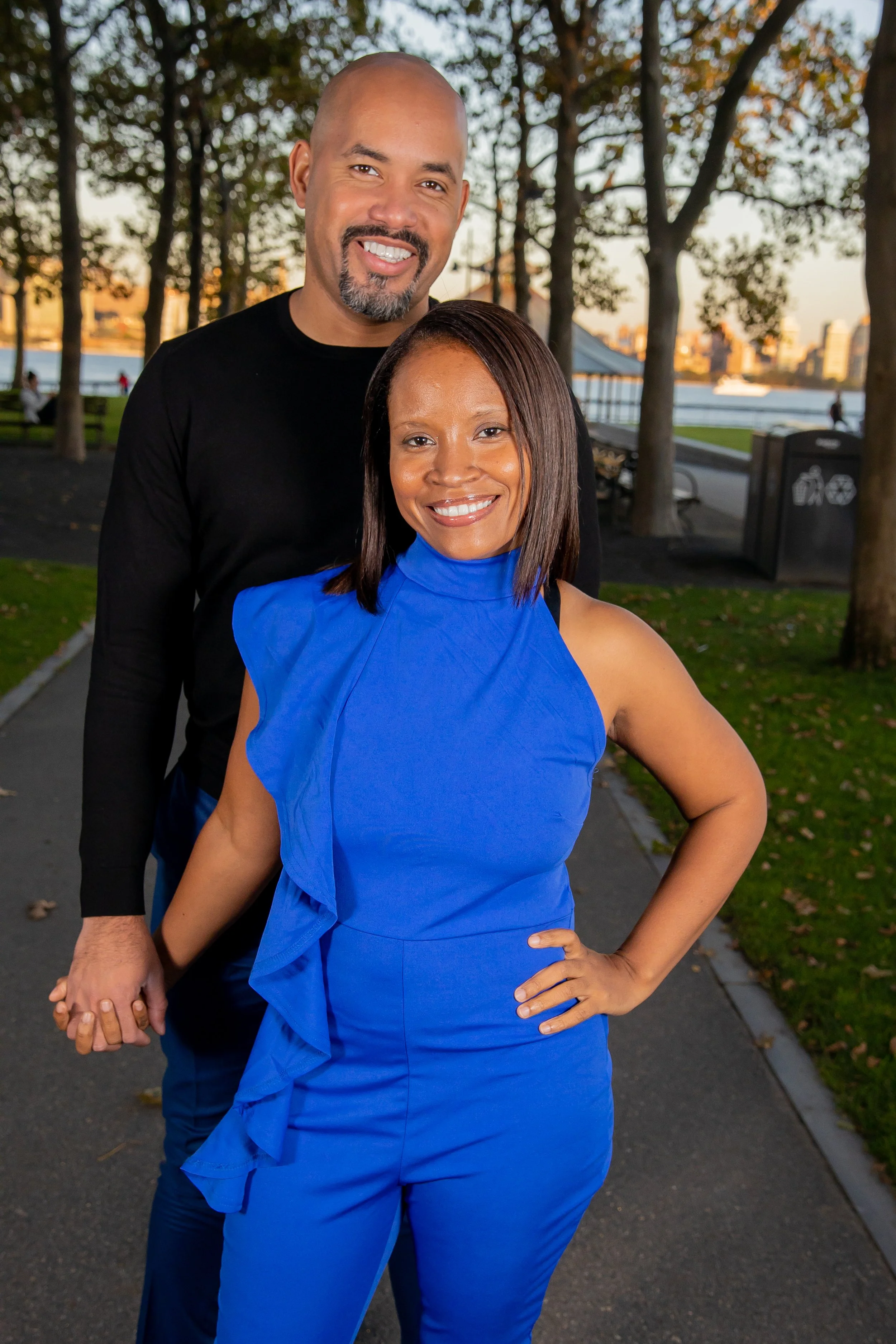 Romantic couple photography in the park at sunset by An Entropy Production, featuring a man and woman holding hands near trees, pathway, and river. Family photography with An Entropy Production