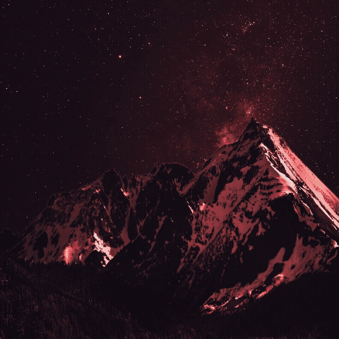 Snow-covered mountain peaks at night with a starry sky and a pinkish hue.