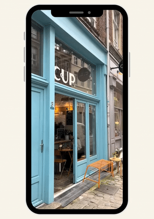 Façade d'un café ou restaurant avec une devanture bleue, grandes fenêtres, et un petit espace extérieur avec des chaises en rotin