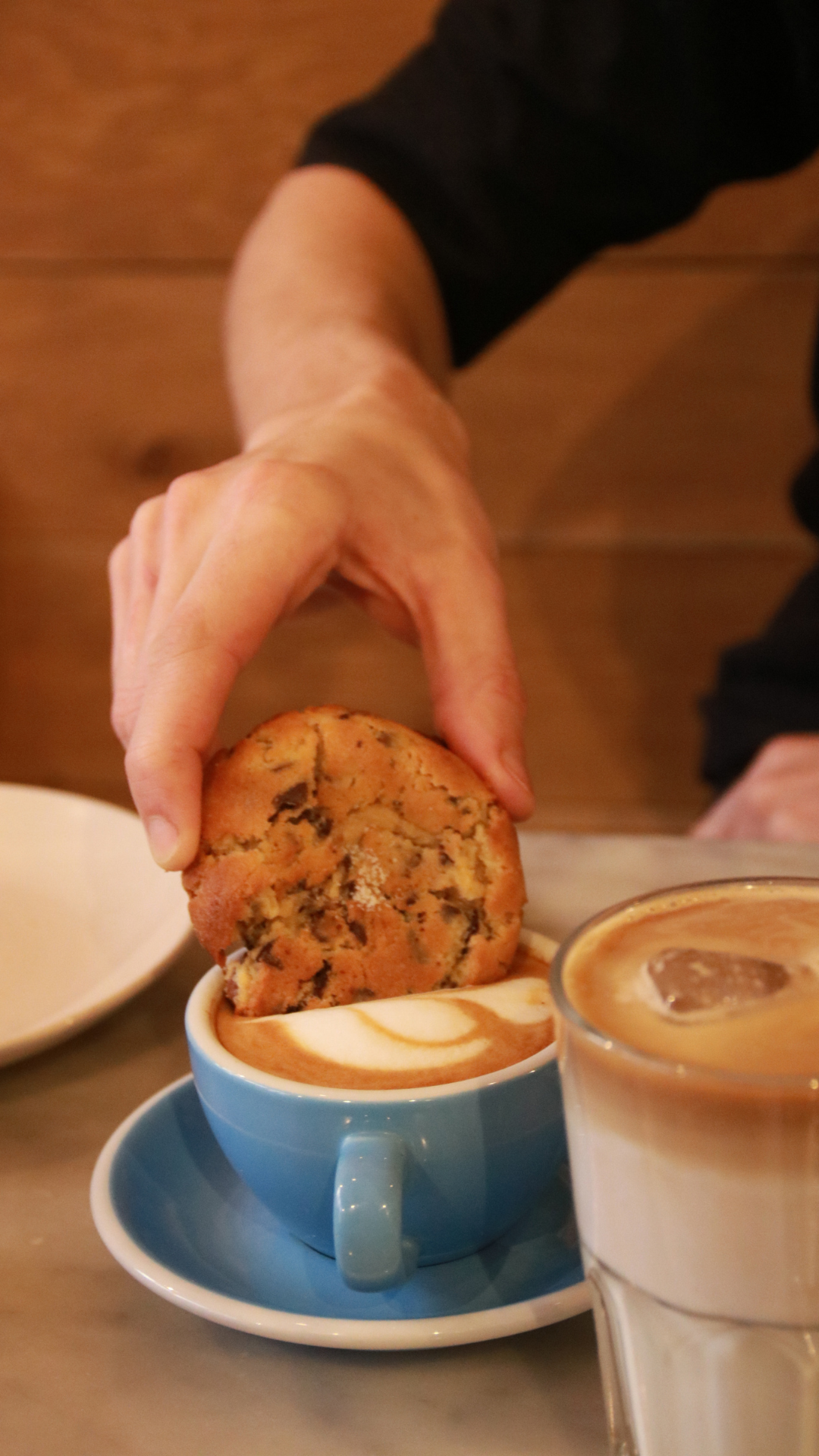 Main tenant un cookie dans une tasse de café au lait, avec un autre verre de café à côté.