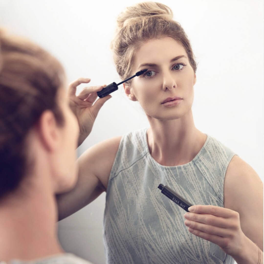 Model applying The Skincare Company Luxury Mascara while looking in a mirror.