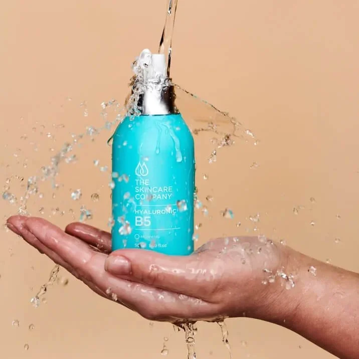The Skincare Company Hyaluronic B5 Serum bottle with flowing water held above an open hand.