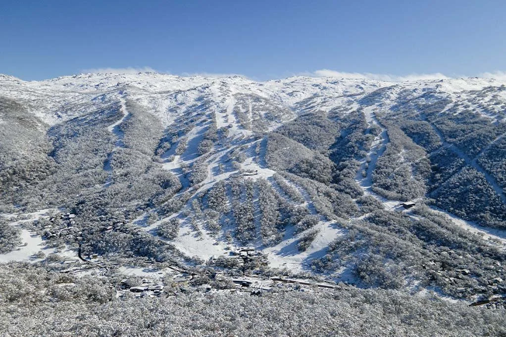 Snow-covered mountain with ski slopes and a few scattered buildings at the base.