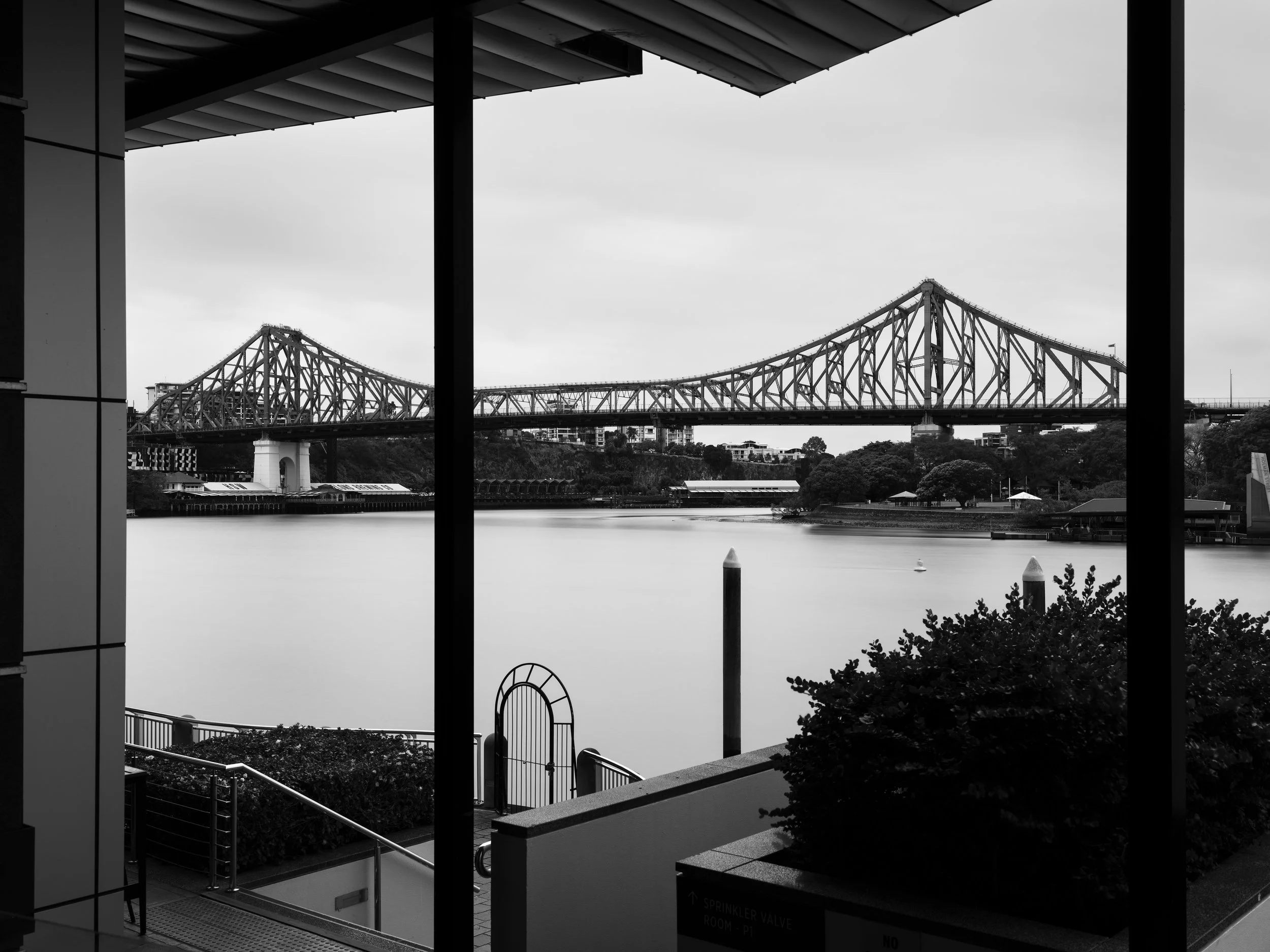 View of a large bridge over a river, seen through a window with vertical and horizontal framing, black and white image.