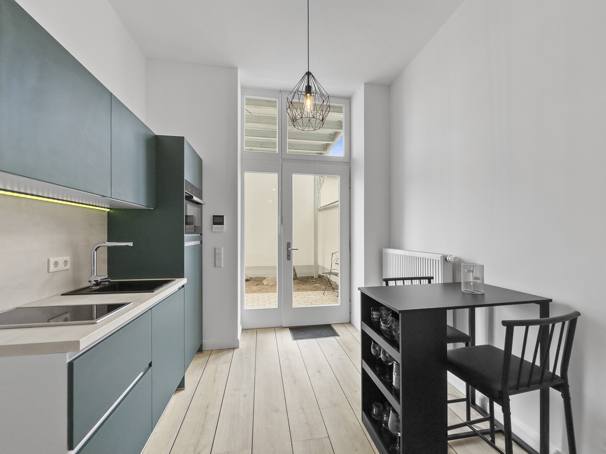 Restaurierte helle und freundliche Einzimmerwohnung mit moderner Einbauküche, Bett, Tresen und TV, Blick auf kleinen ebenerdigen Außenbereich durch Glastür