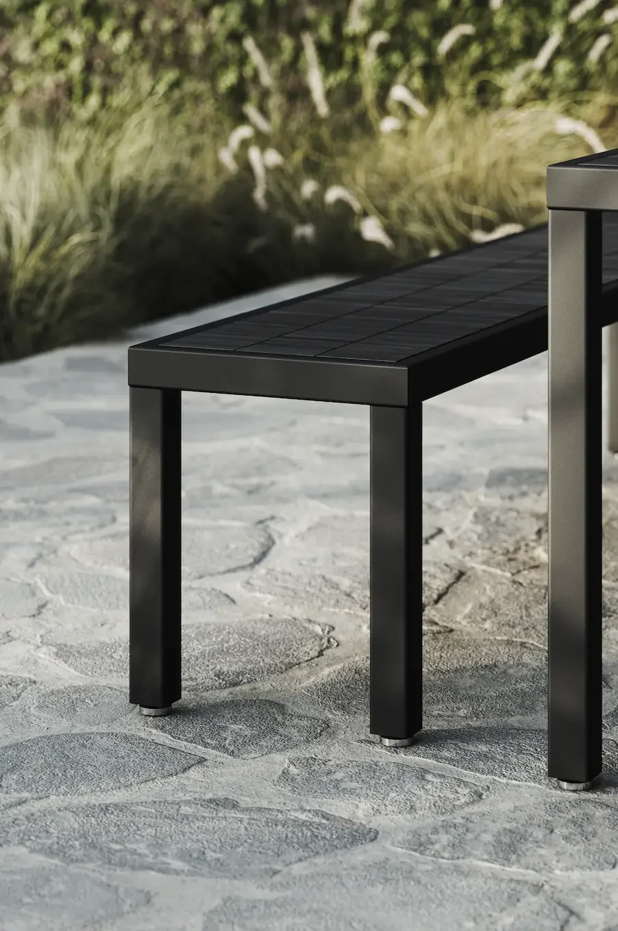 Metal outdoor table with black top, situated on a stone patio with greenery in the background.