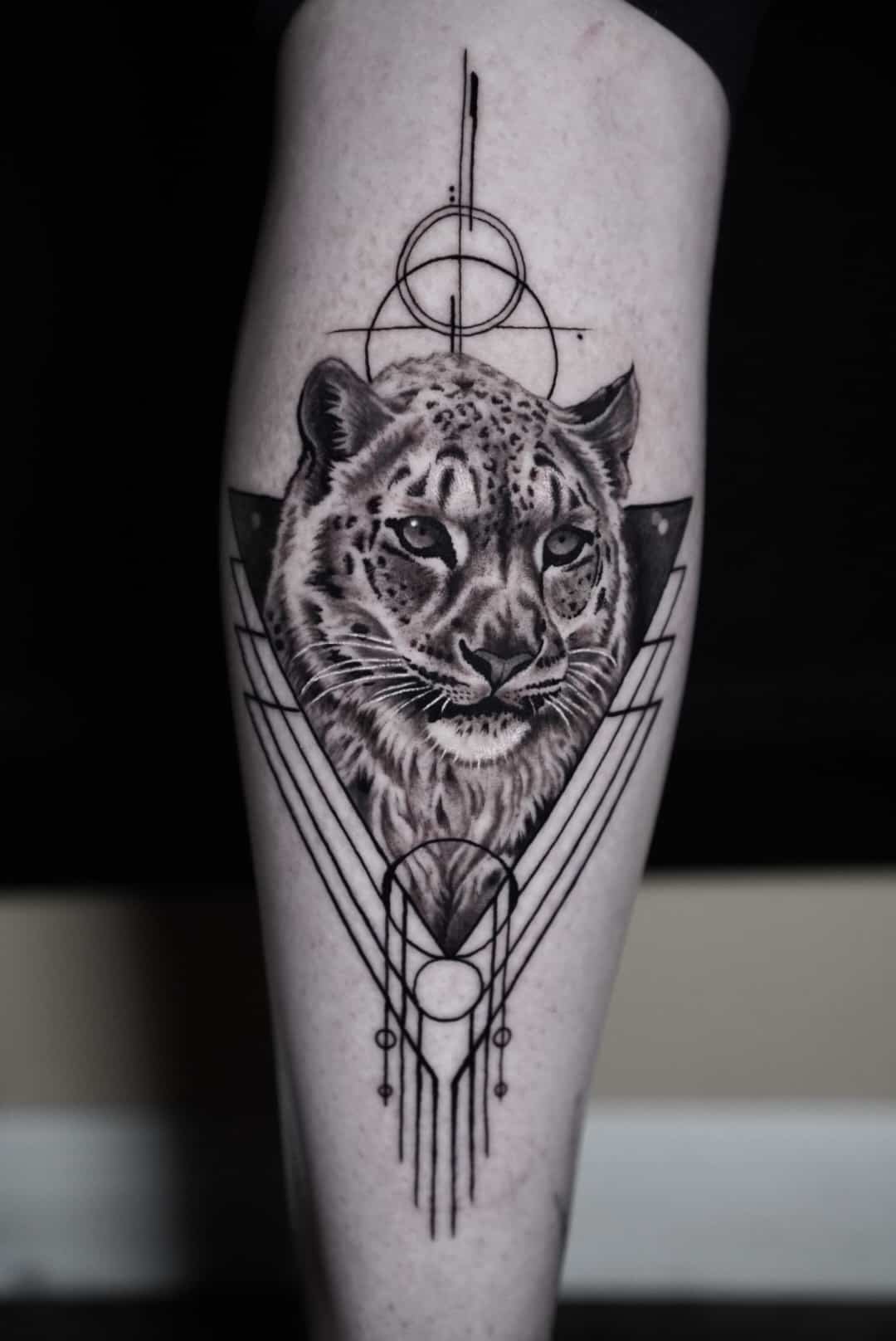 Tattoo of a leopard's face with geometric designs and circles above and below.