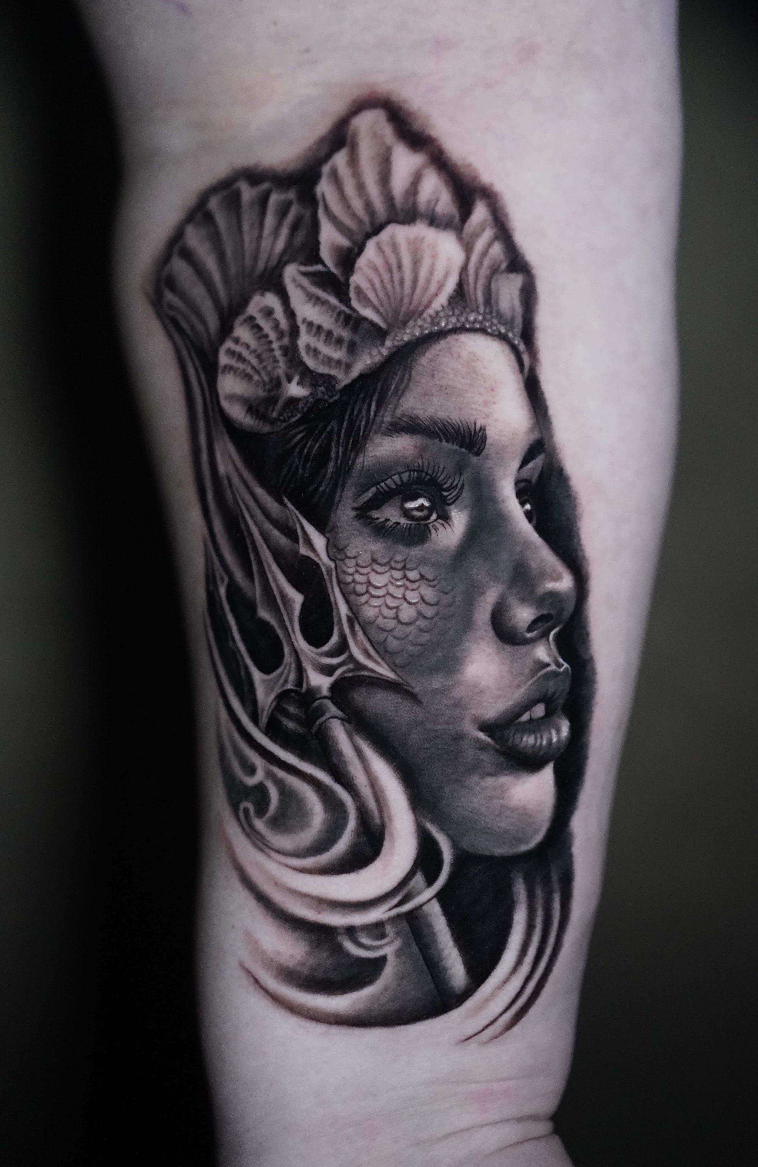 Black and gray tattoo of a woman's face with seashells and fish scales, featuring detailed shading and realistic features.