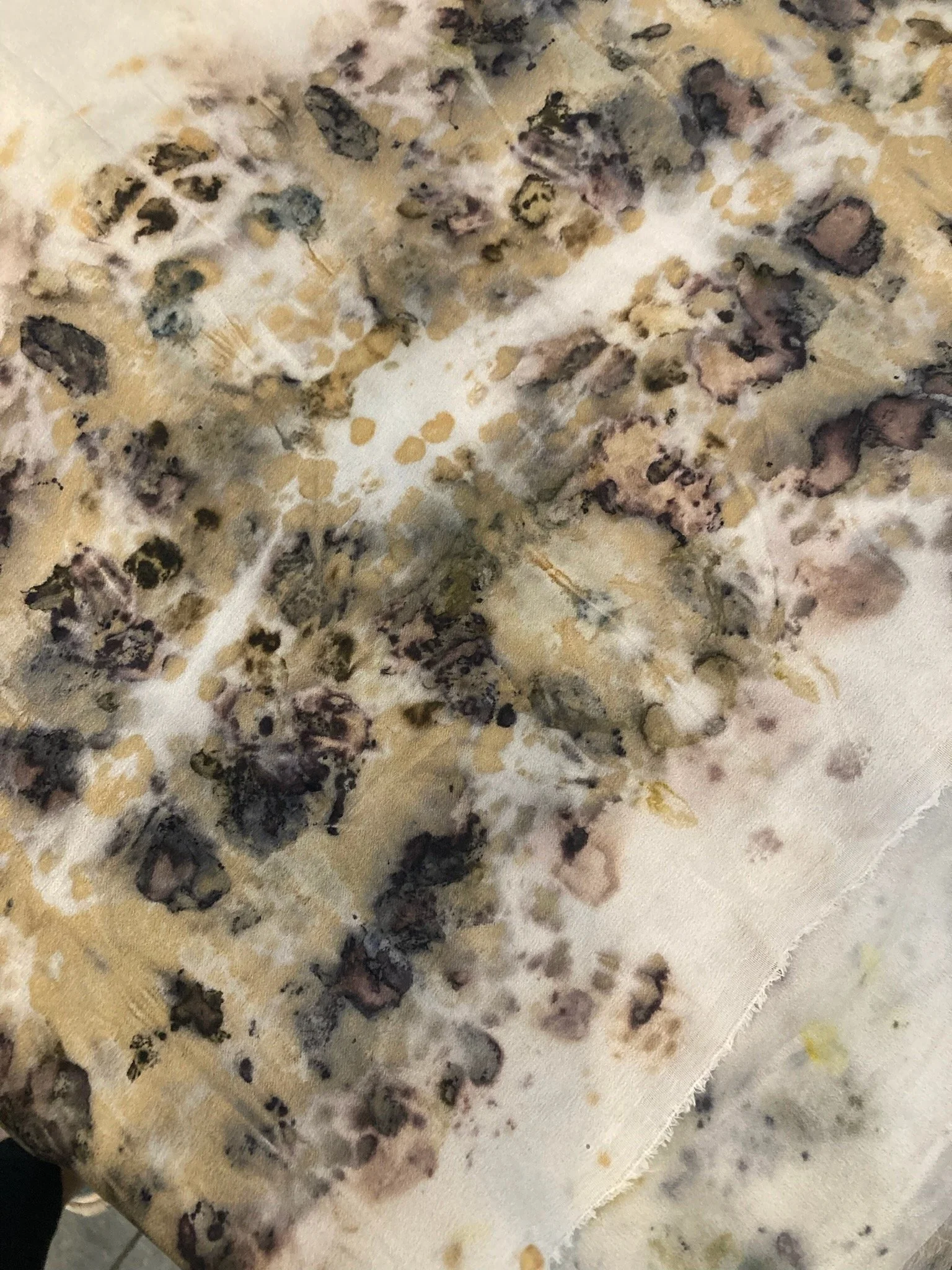 A close-up of fabric with a watercolor-like floral pattern in soft beige, purple, gray, and yellow tones.