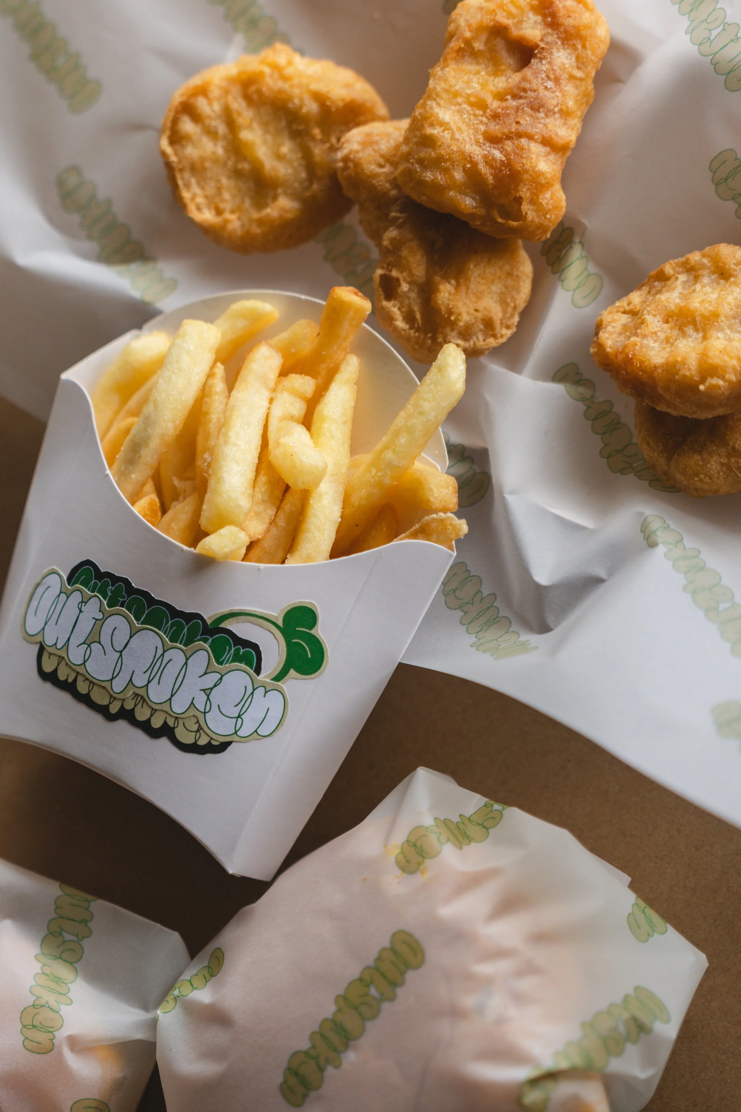 A serving of fried chicken pieces with a portion of French fries in branded paper containers on a table.