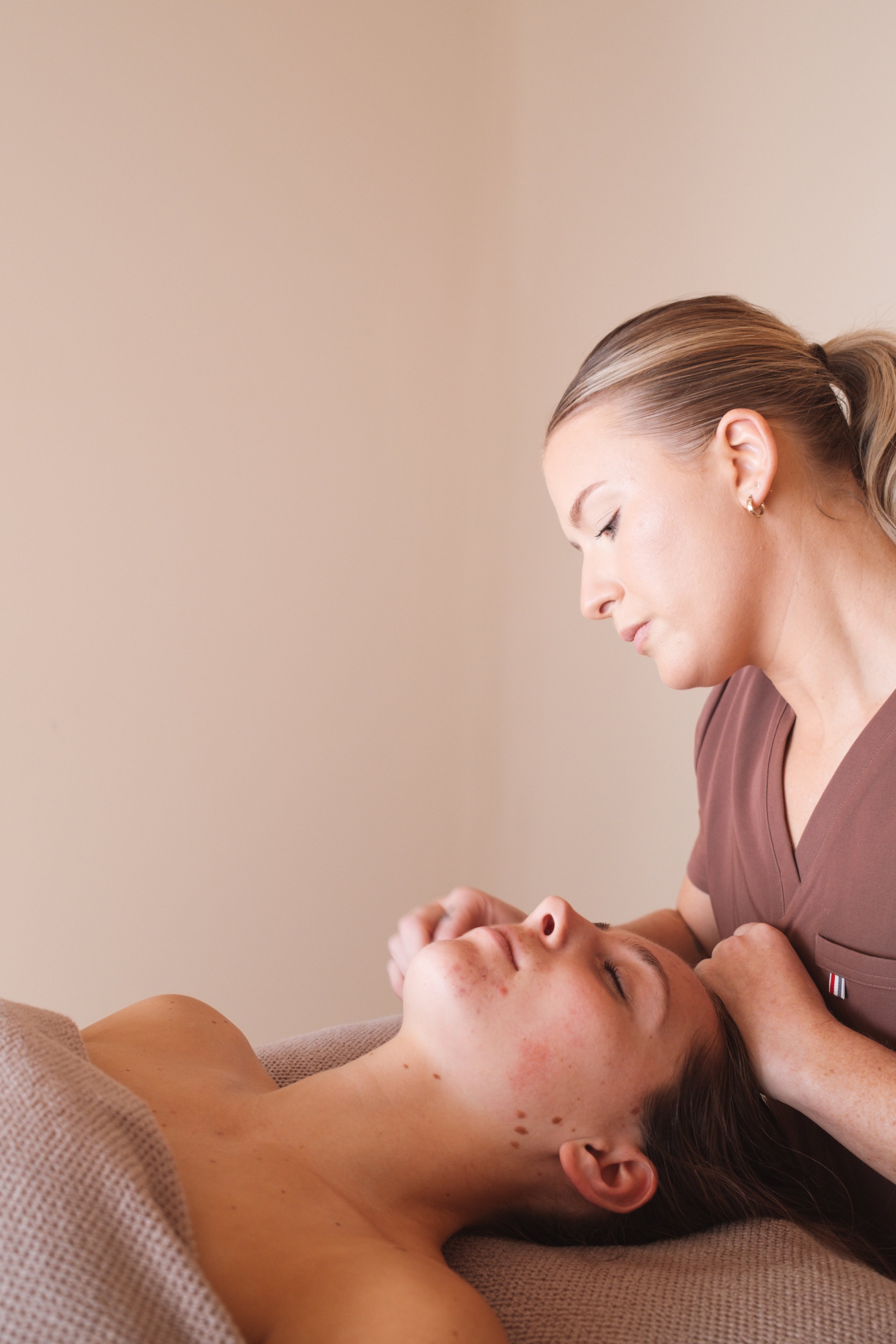 A woman receiving facial massage from a professional skincare specialist in a spa setting.