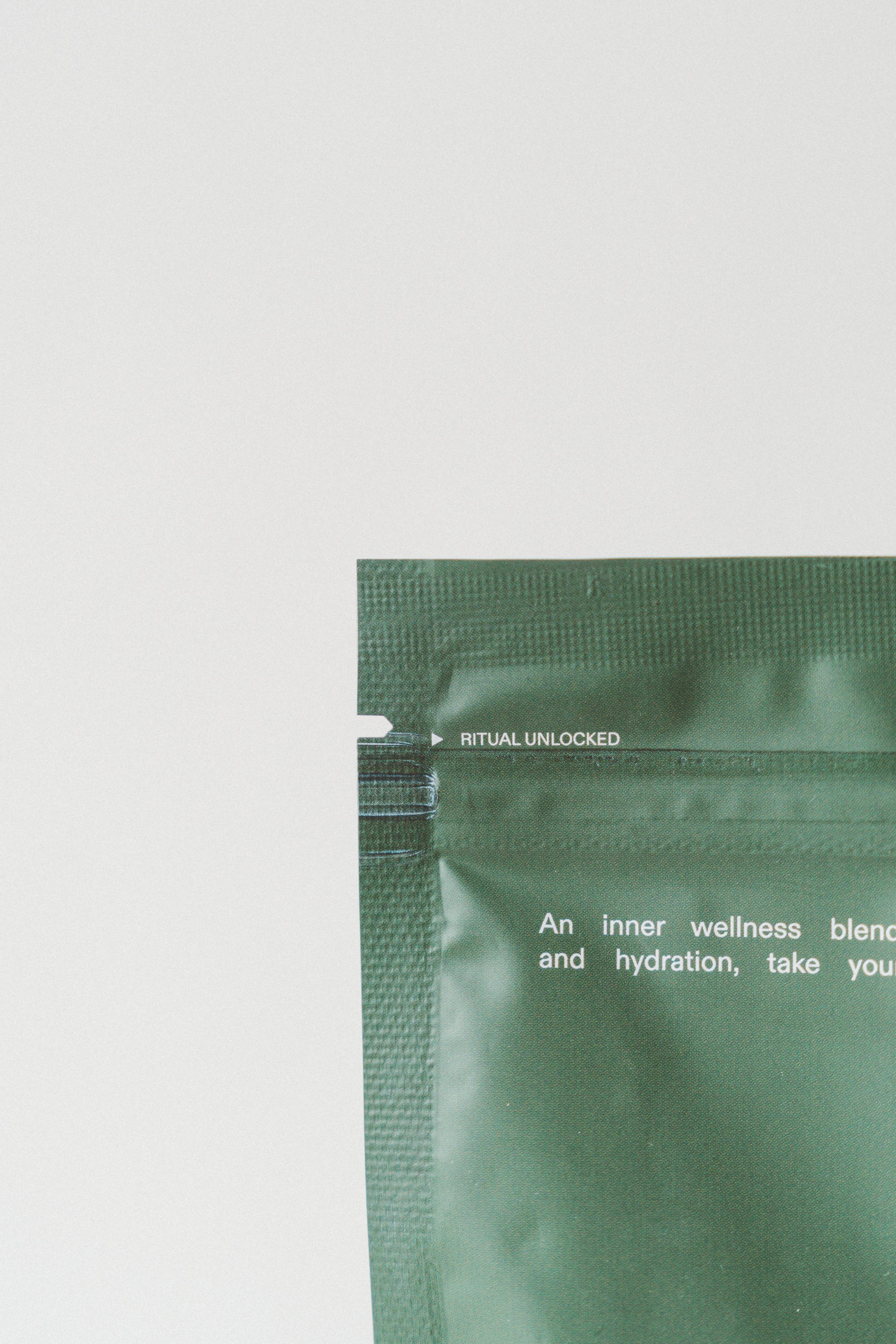 Close-up of a green facial skincare product packaging with partial text 'RITUAL UNLOCKED' and some descriptive text about wellness and hydration.