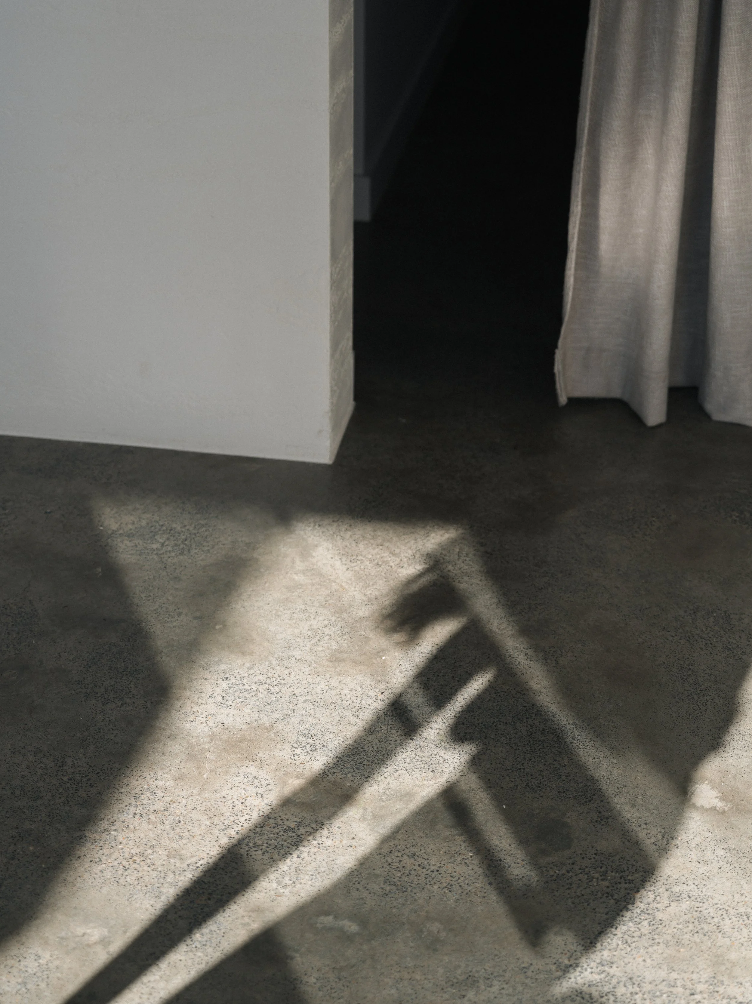 Shadow of a person taking a photo, with stripes on the floor and curtain to the right, in a room with a white wall and staircase in the background.