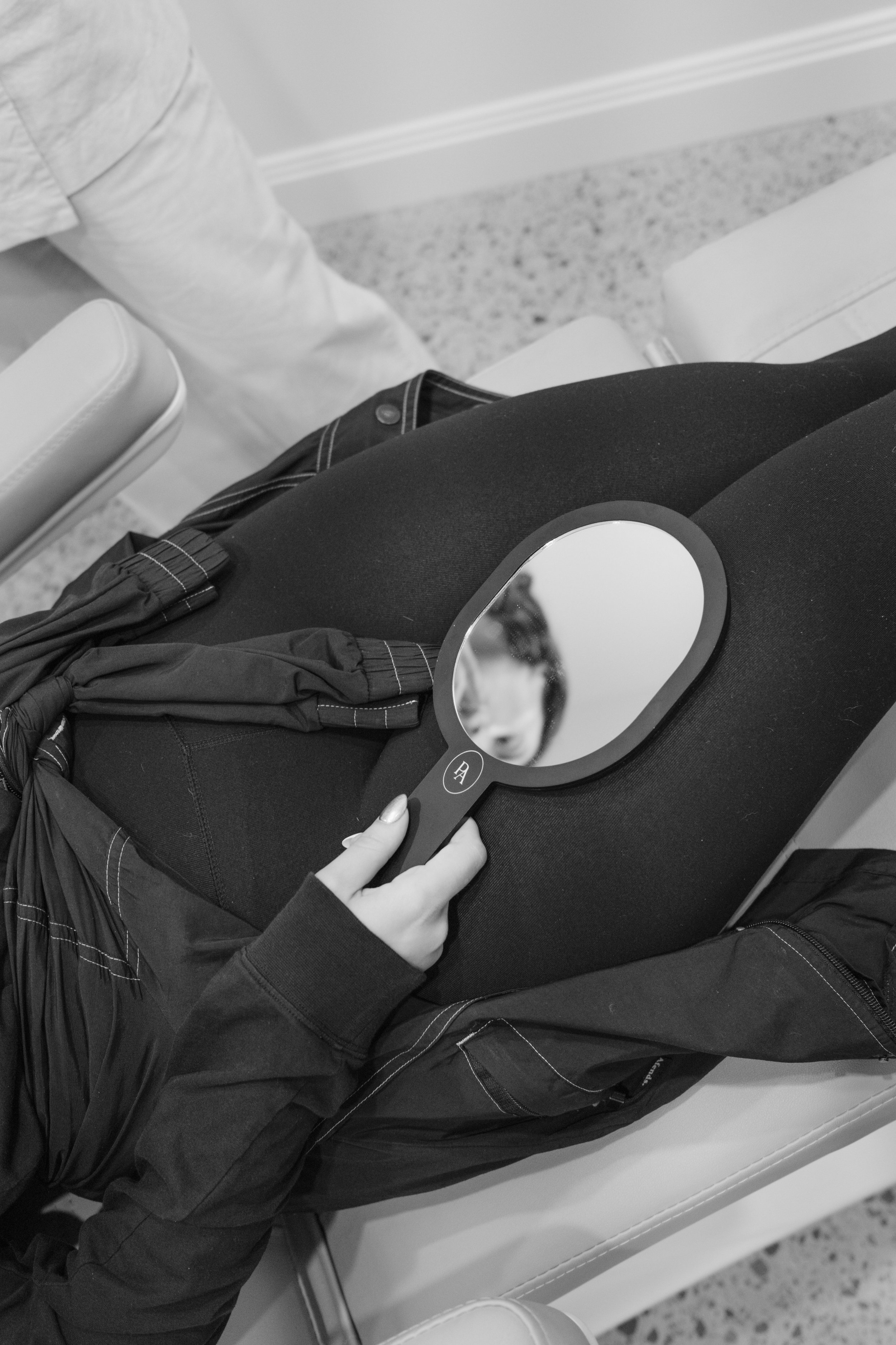 Person using a handheld mirror to check their reflection while sitting on a padded bench.