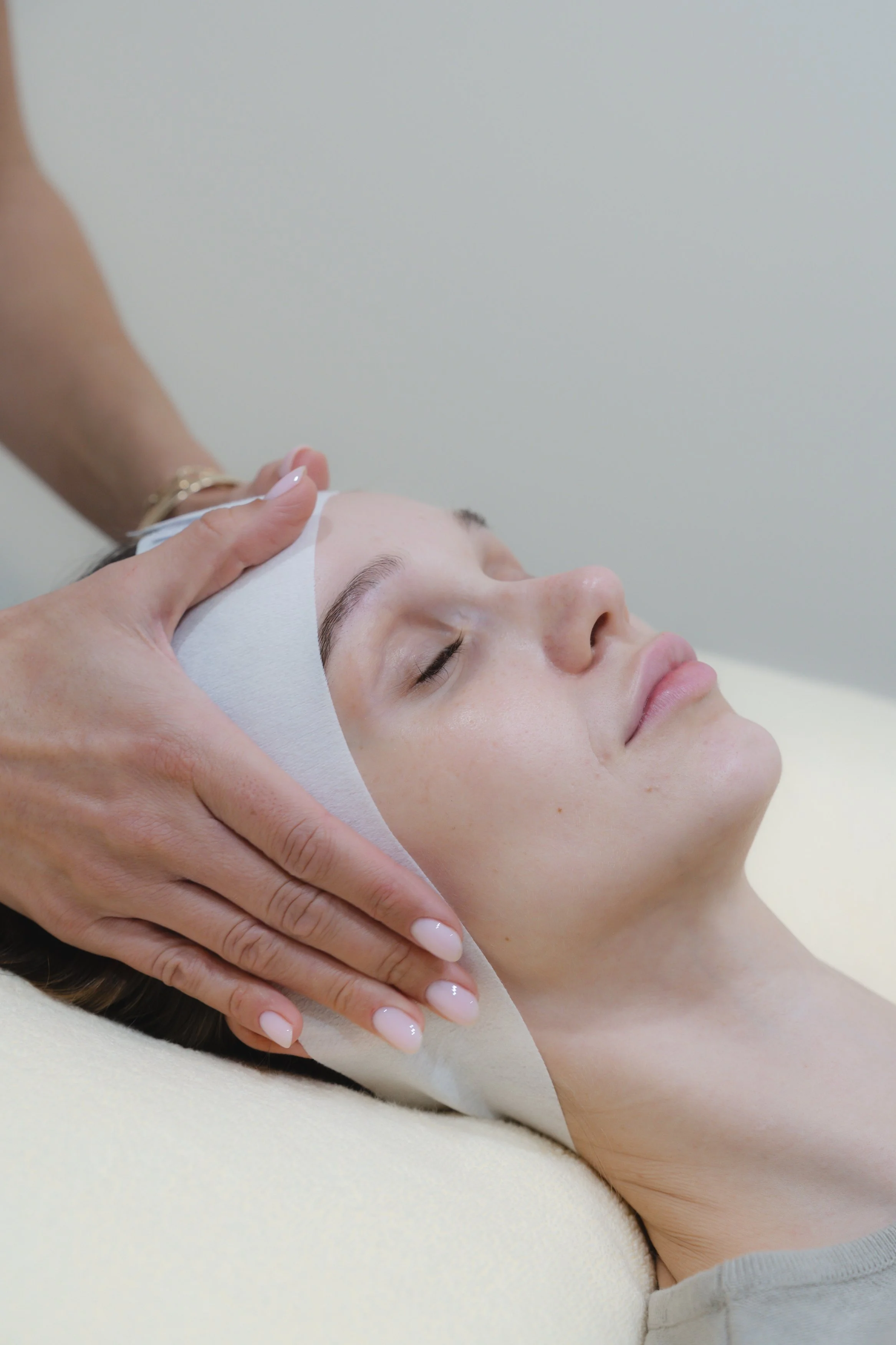 A woman receives a facial massage while lying down with her eyes closed.