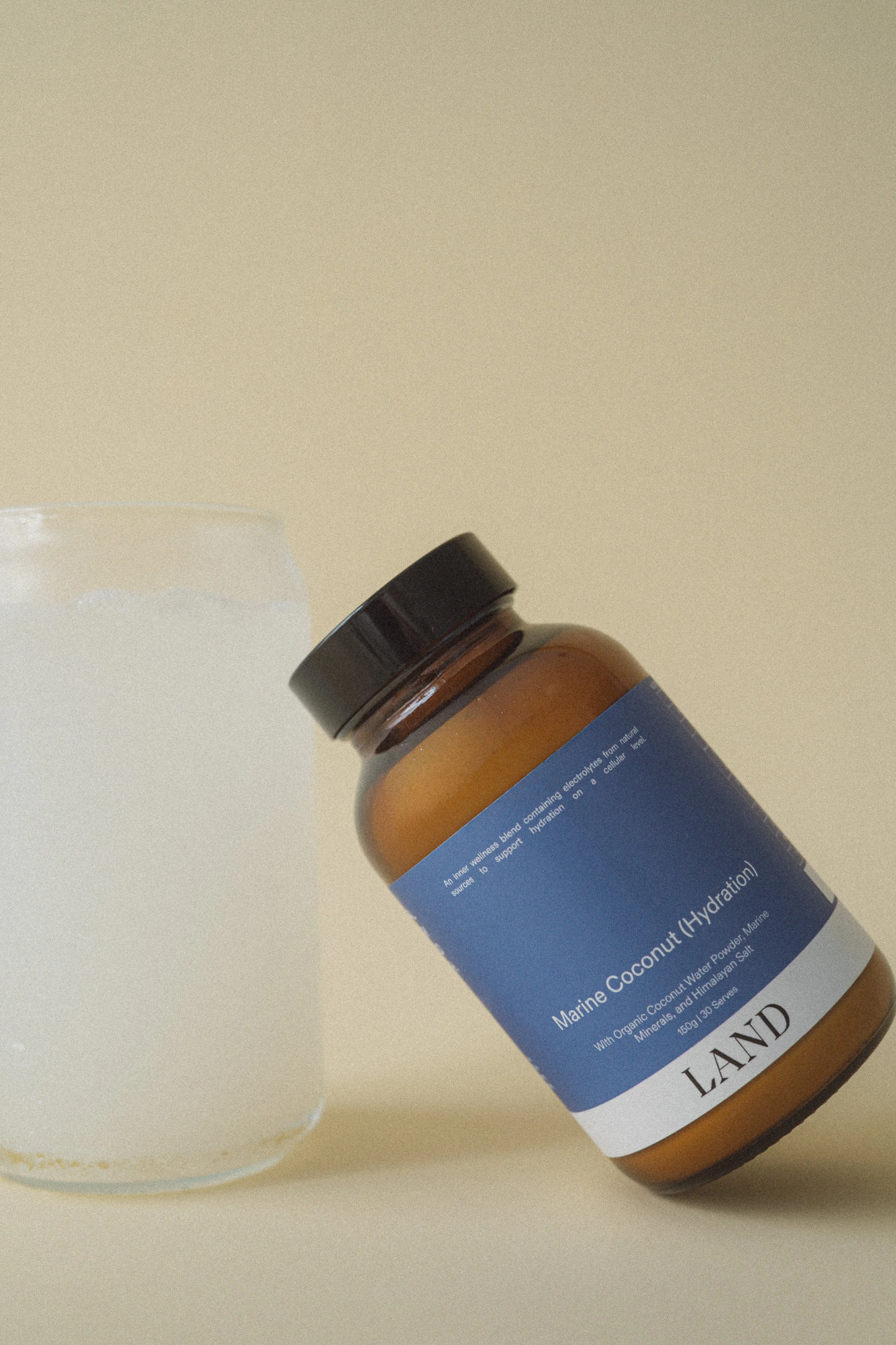 A bottle of marine coconut water powder with a blue label, placed on a beige surface next to a white container.