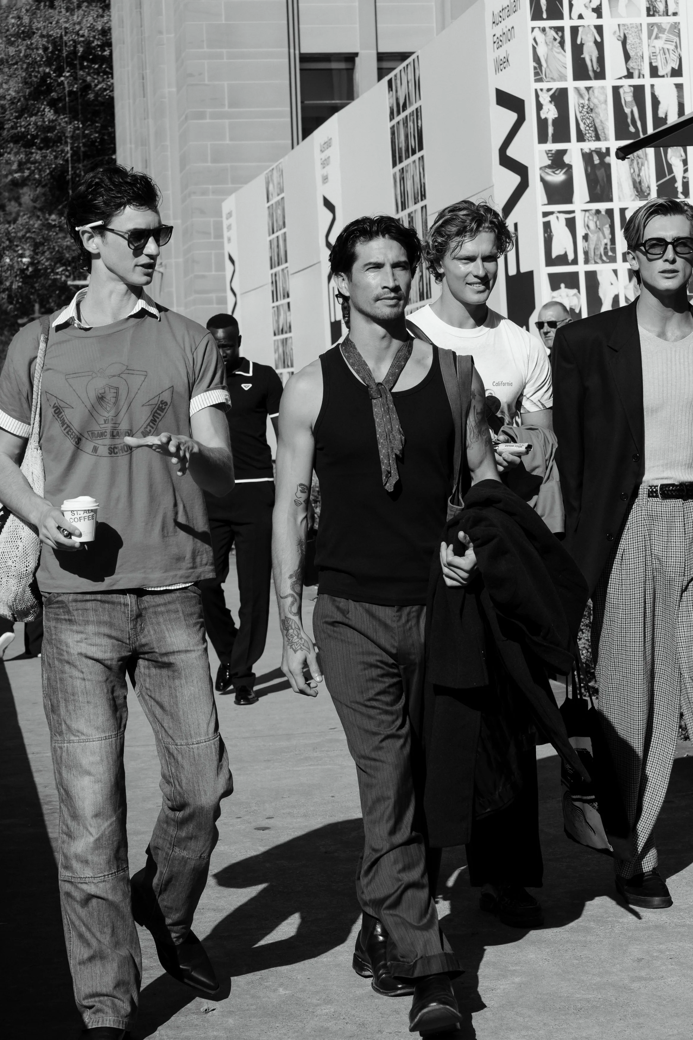 Black and white photo of a group of casually dressed people walking outdoors in front of a building with large sign that reads 'Australian Fashion Week.'