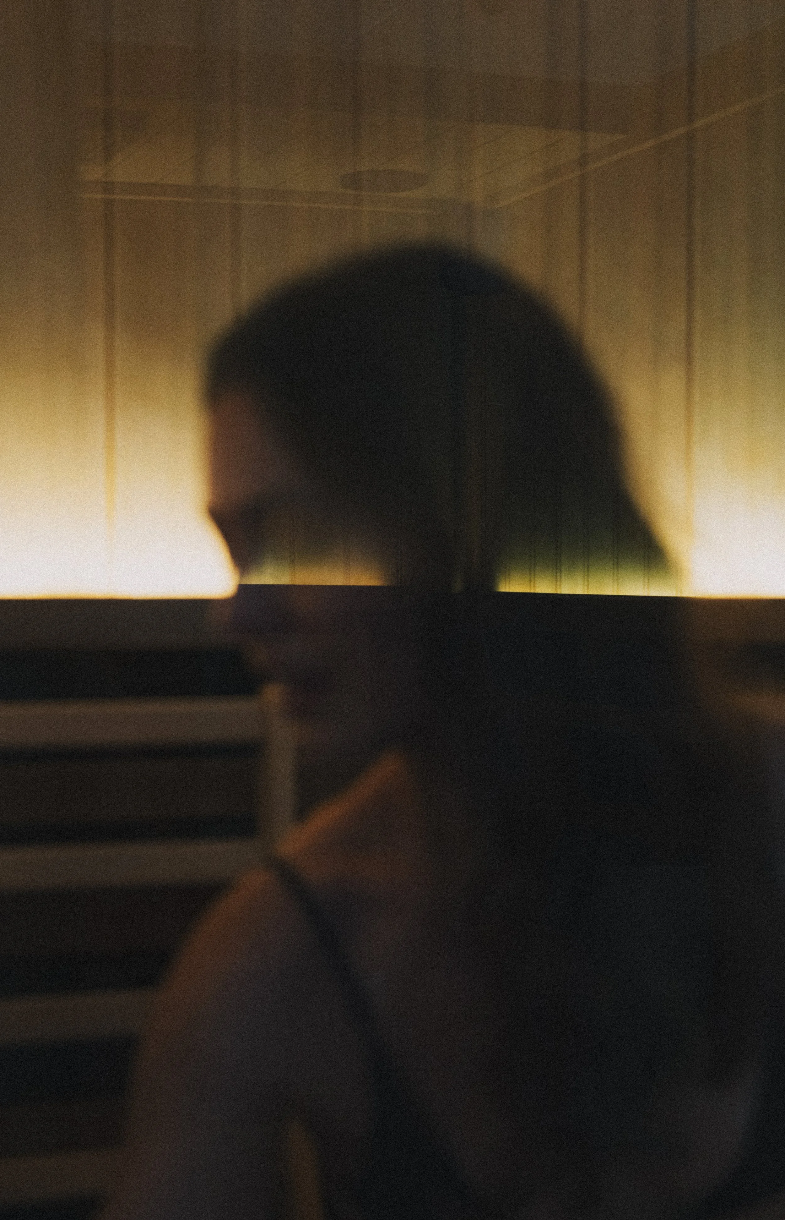 The image shows a blurred reflection of a person's head on a glass or mirror, with a scene of a room and a grid-like ceiling pattern in the background.