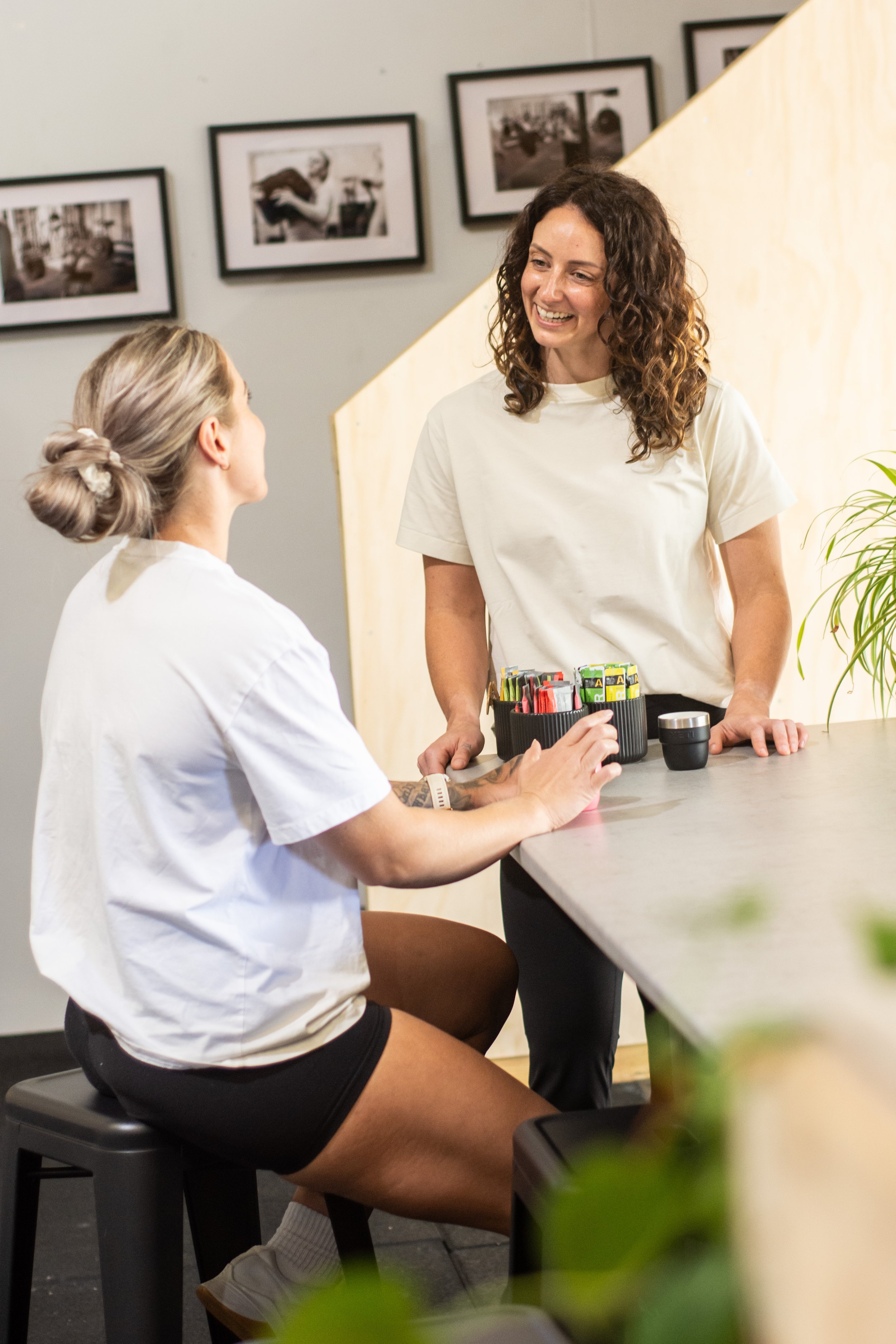 Female Physiotherapist with curly hair speaking to a patient whilst drinking coffee