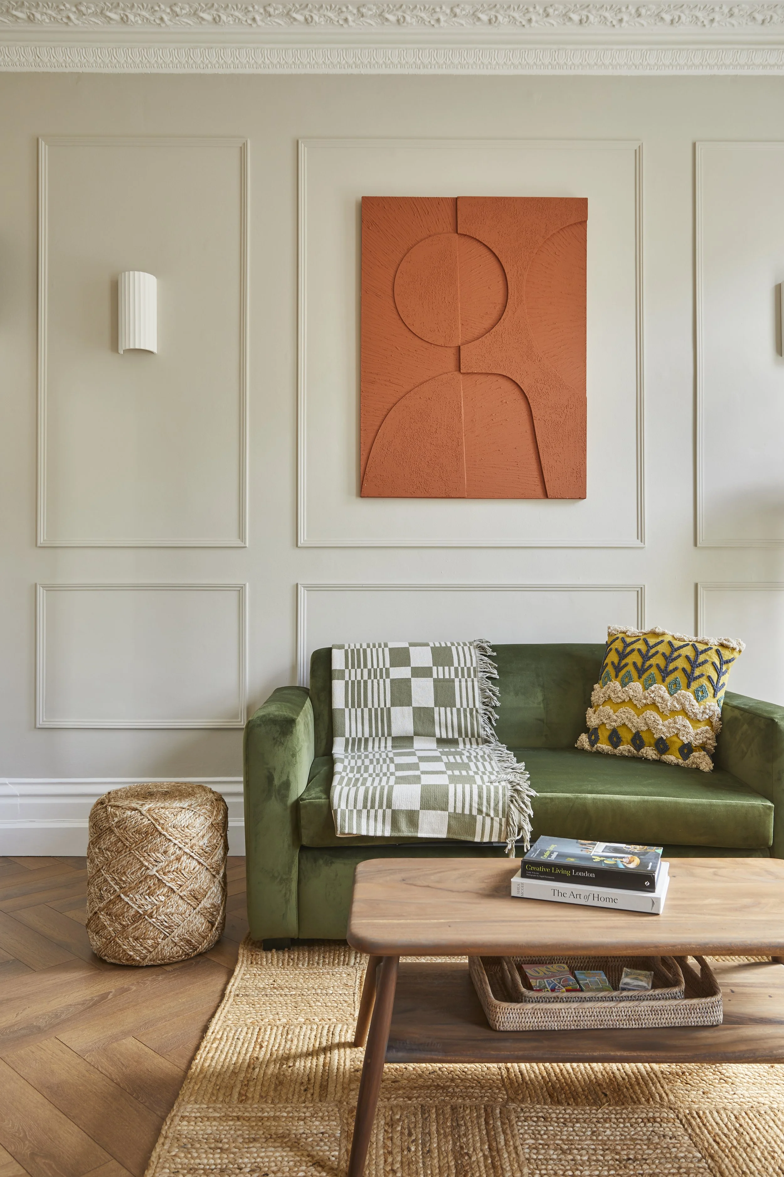 Living room with a green velvet sofa, wooden coffee table, woven pouf, wall art, and decorative pillows.
