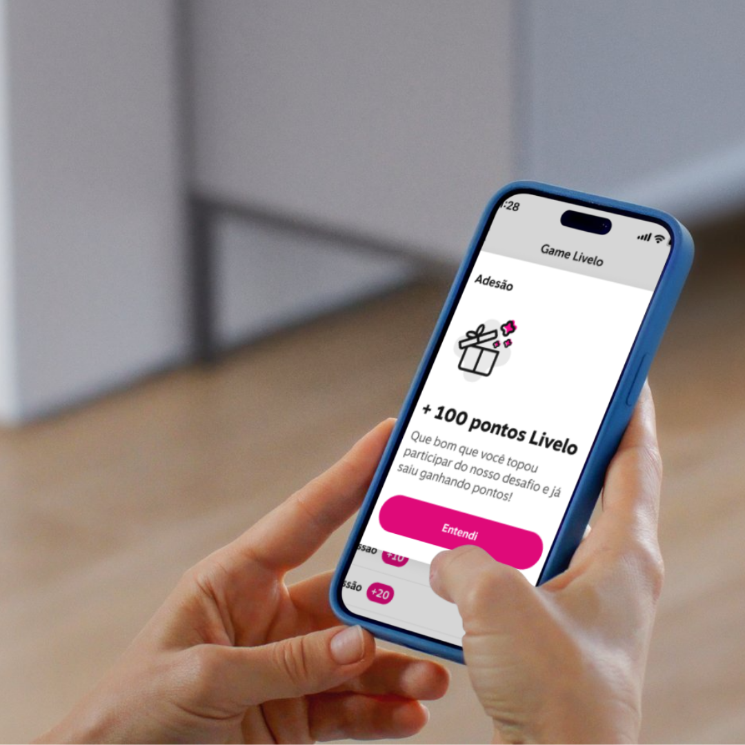 Close-up of a person holding a smartphone displaying a game reward screen with a gift icon, pink button labeled 'Entendi,' and text indicating 100 points earned.