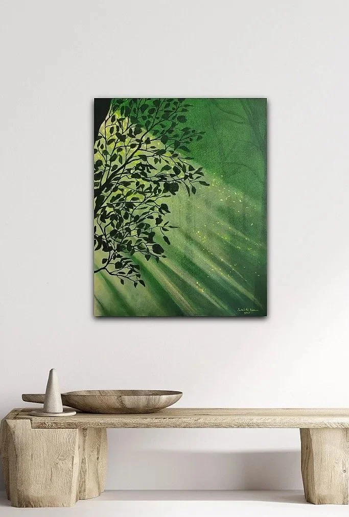 A green abstract artwork depicting a tree silhouette against a vibrant green background with light streaks and sparkles, hanging on a white wall above a rustic wooden table with a bowl and a small cone-shaped decorative object.