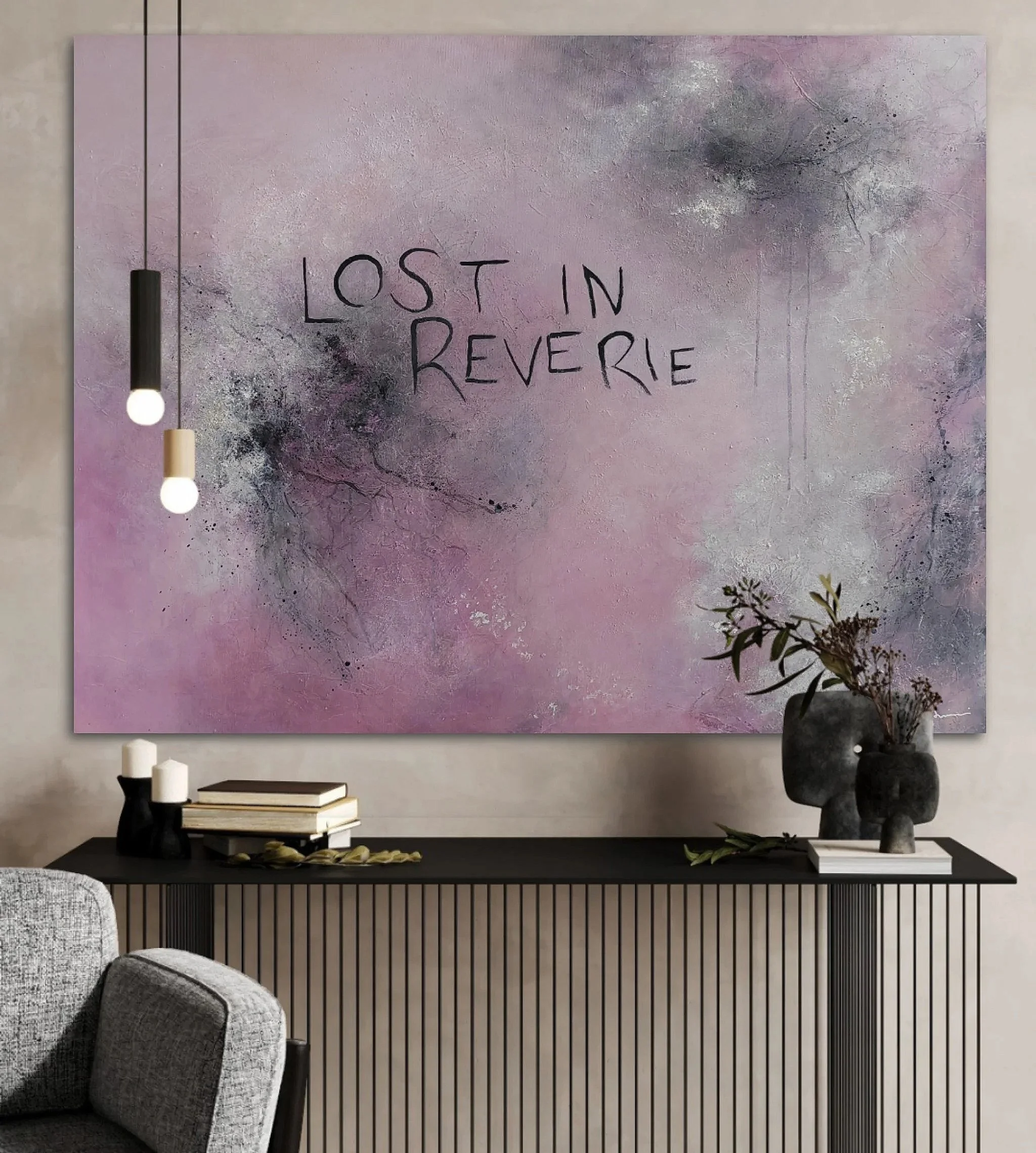 Modern living room with a large abstract pink and gray painting titled 'Lost in Reverie' on the wall, two hanging pendant lights in black and beige, a black console table holding candles, books, and a decorative vase with greenery, and a gray upholstered armchair.
