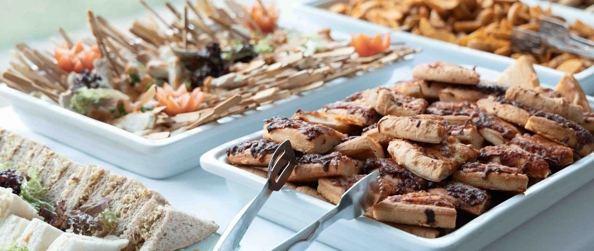 Tray of grilled chicken drumsticks and a tray of seafood salad with vegetables at a buffet.