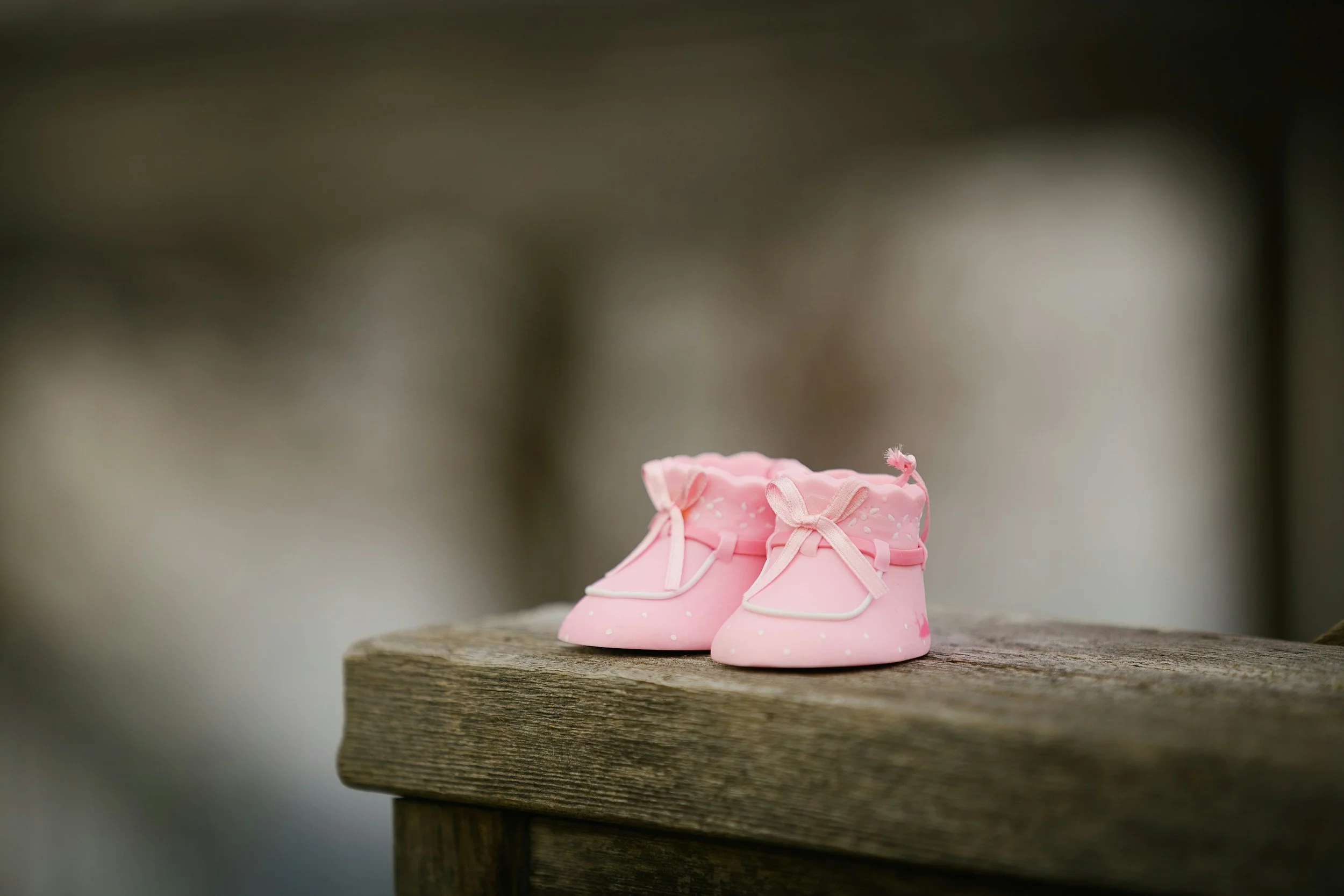 A pair of pink baby shoes with white polka dots and bow laces sitting on a weathered wooden surface.
