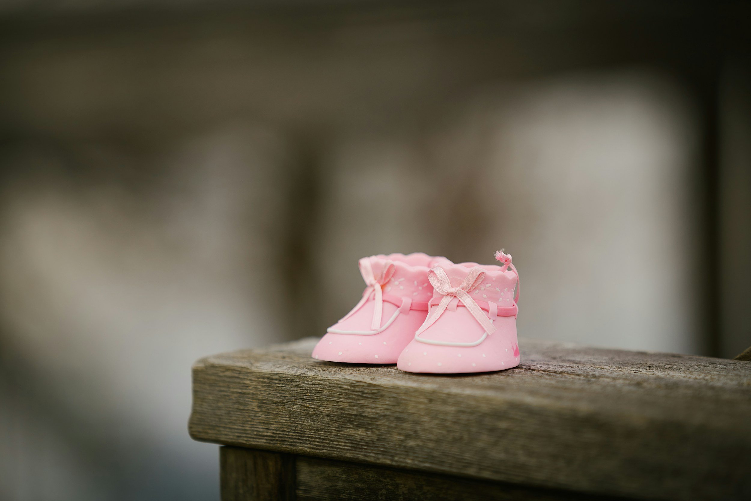 A pair of small pink baby shoes with white laces resting on a wooden surface.