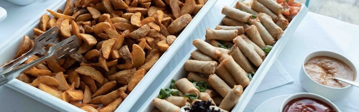 Buffet tray with fried potato wedges and spring rolls, accompanied by bowls of dipping sauce.