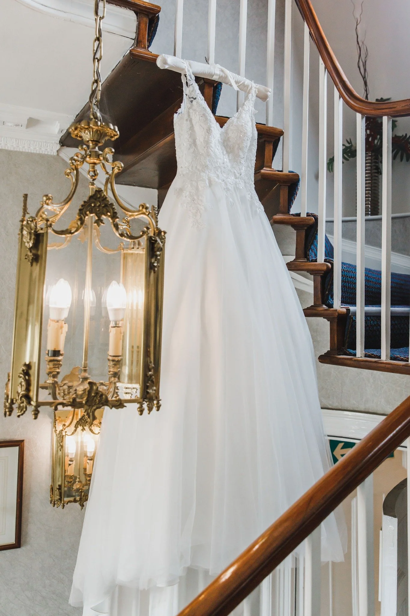A white bridal wedding dress hanging from a railing on a staircase.