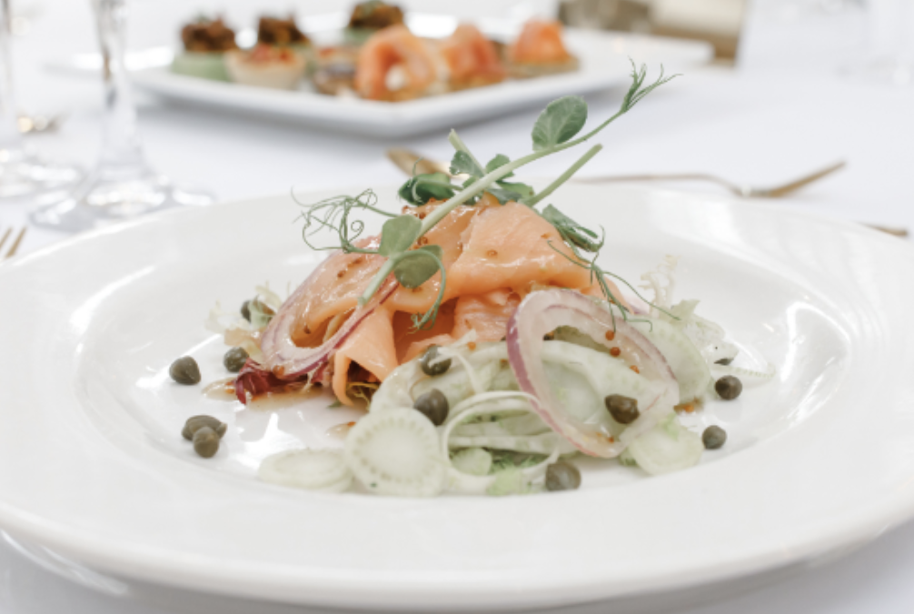 Salmon gravlax with thinly sliced cucumbers, red onions, capers, and microgreens on a white plate.