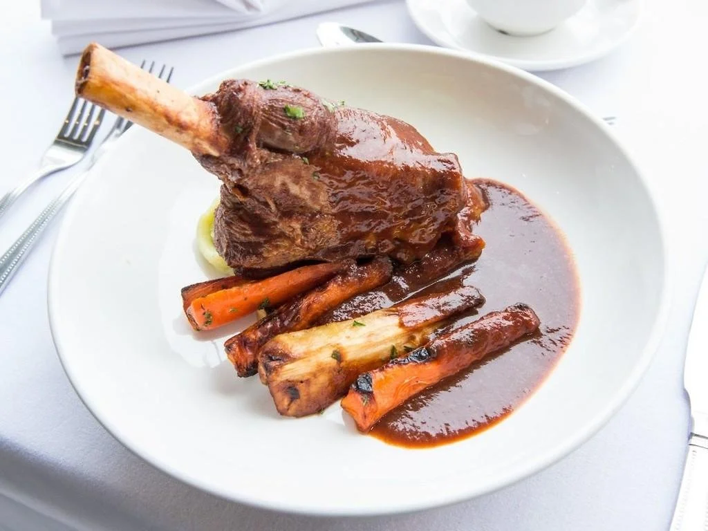 Roast lamb shank with vegetables and gravy on a white plate