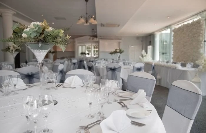 Elegant banquet hall with white tablecloths, floral centerpieces, and neatly arranged glassware and silverware for a formal event.