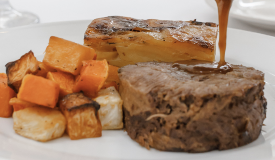 Steak with gravy, roasted potatoes, and sweet potatoes on a white plate.