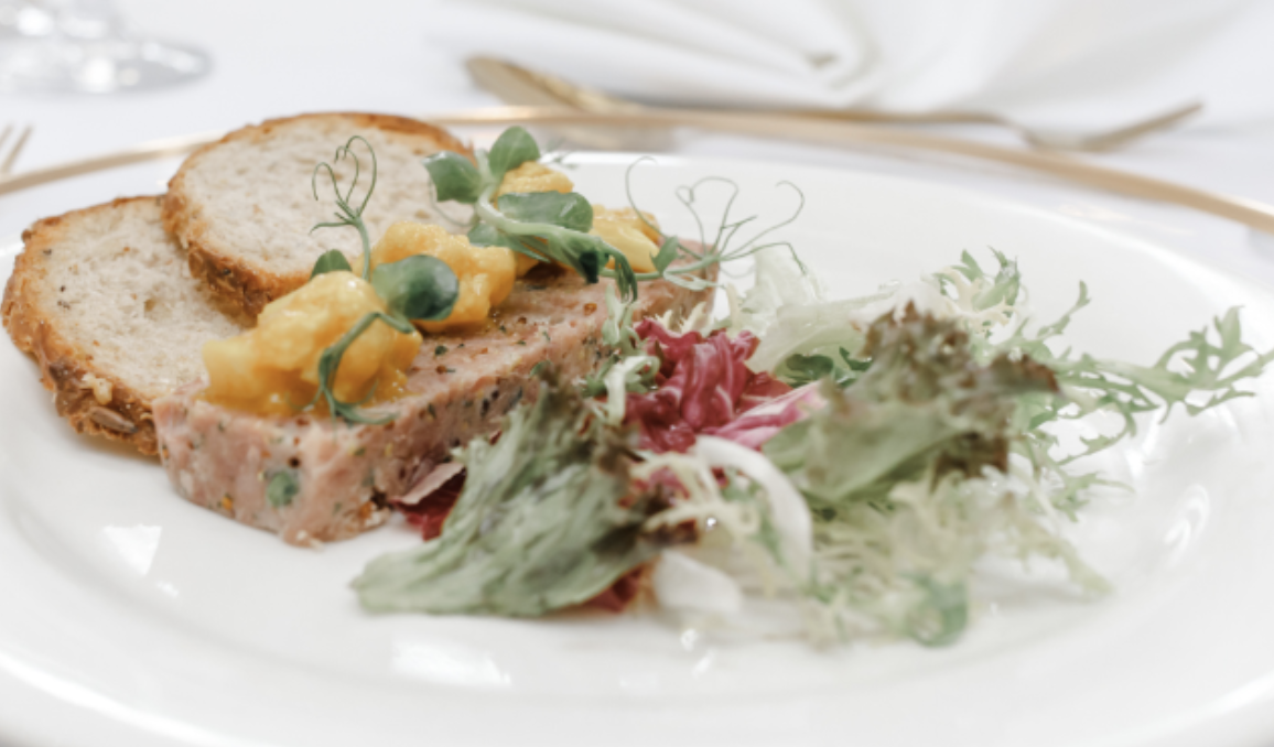 Salad with leafy greens, pate with yellow garnish and slices of bread on a white plate