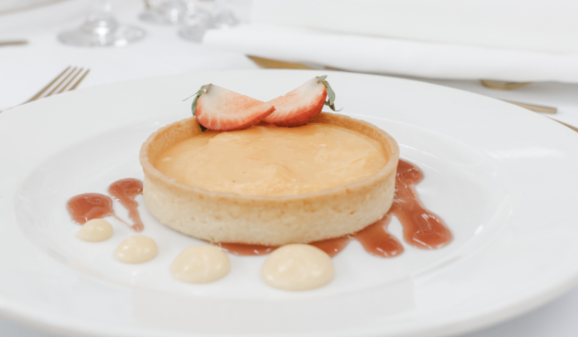 Cheesecake with strawberry slices and decorative sauces on a white plate.