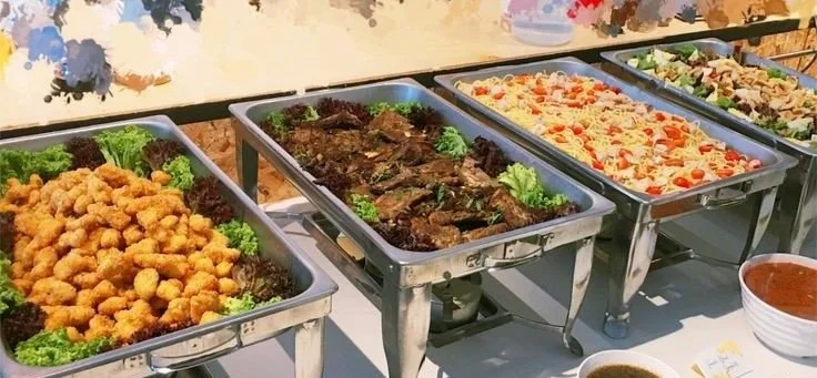 Buffet with trays of fried chicken, cooked beef, pasta salad, and vegetable salad.