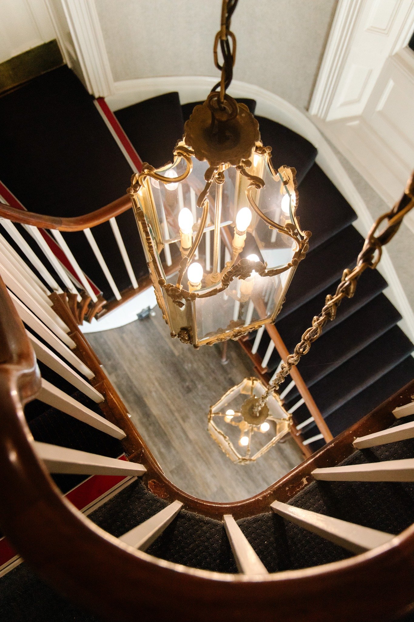 Looking down a spiral staircase with hanging chandeliers illuminating the stairwell.