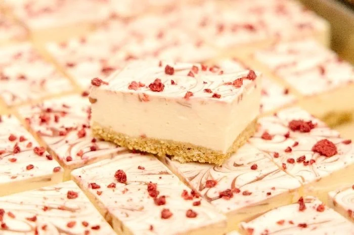 A close-up of a sliced cheesecake on a marble surface, topped with red berries and raspberry sauce drizzles.