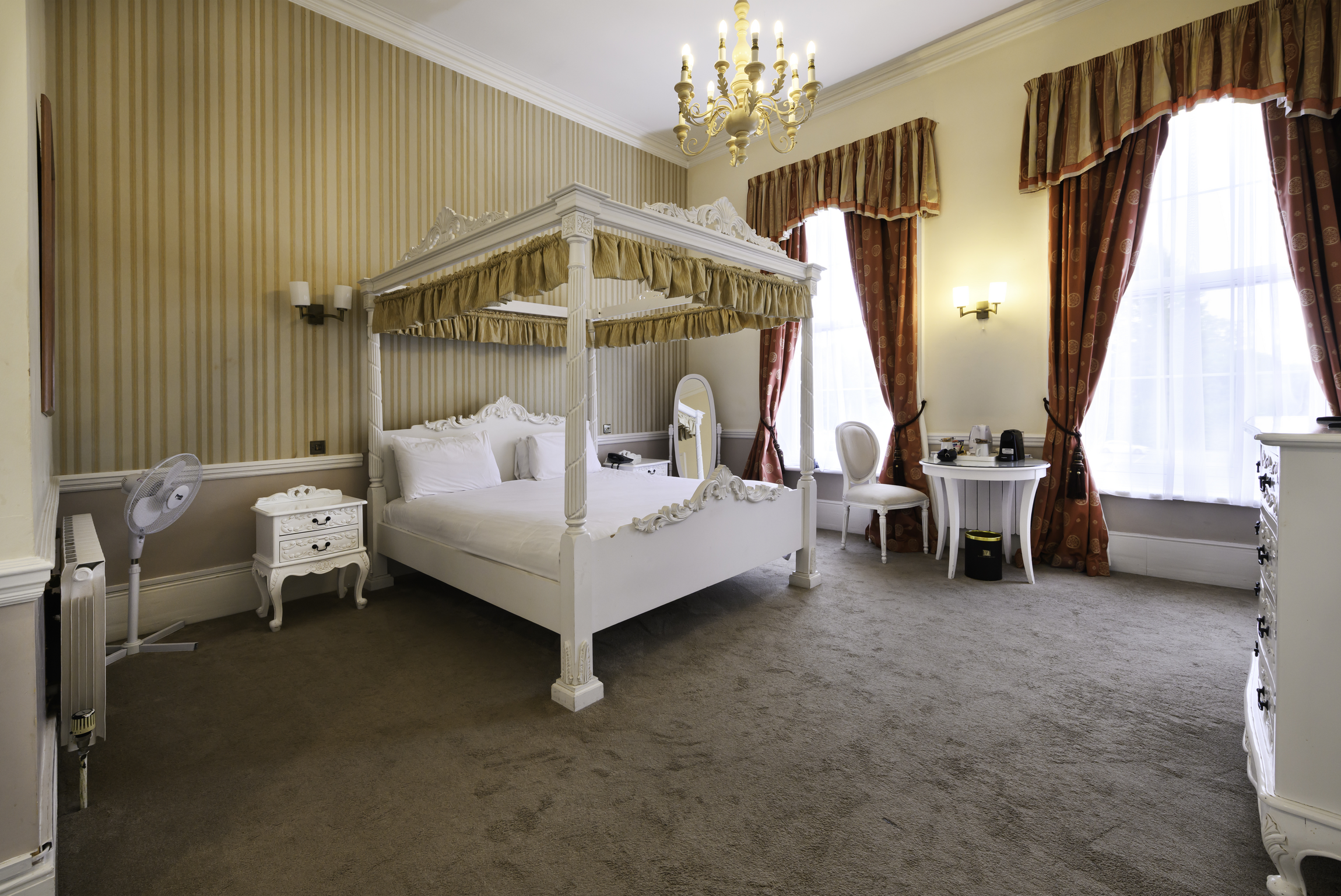 A bedroom with a four-poster bed, side tables, a sitting area, and large windows with curtains.