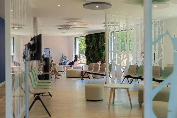 Salle d'attente du Centre Main Morbihan, avec des fauteuils, un mur végétal, des personnes en conversation.