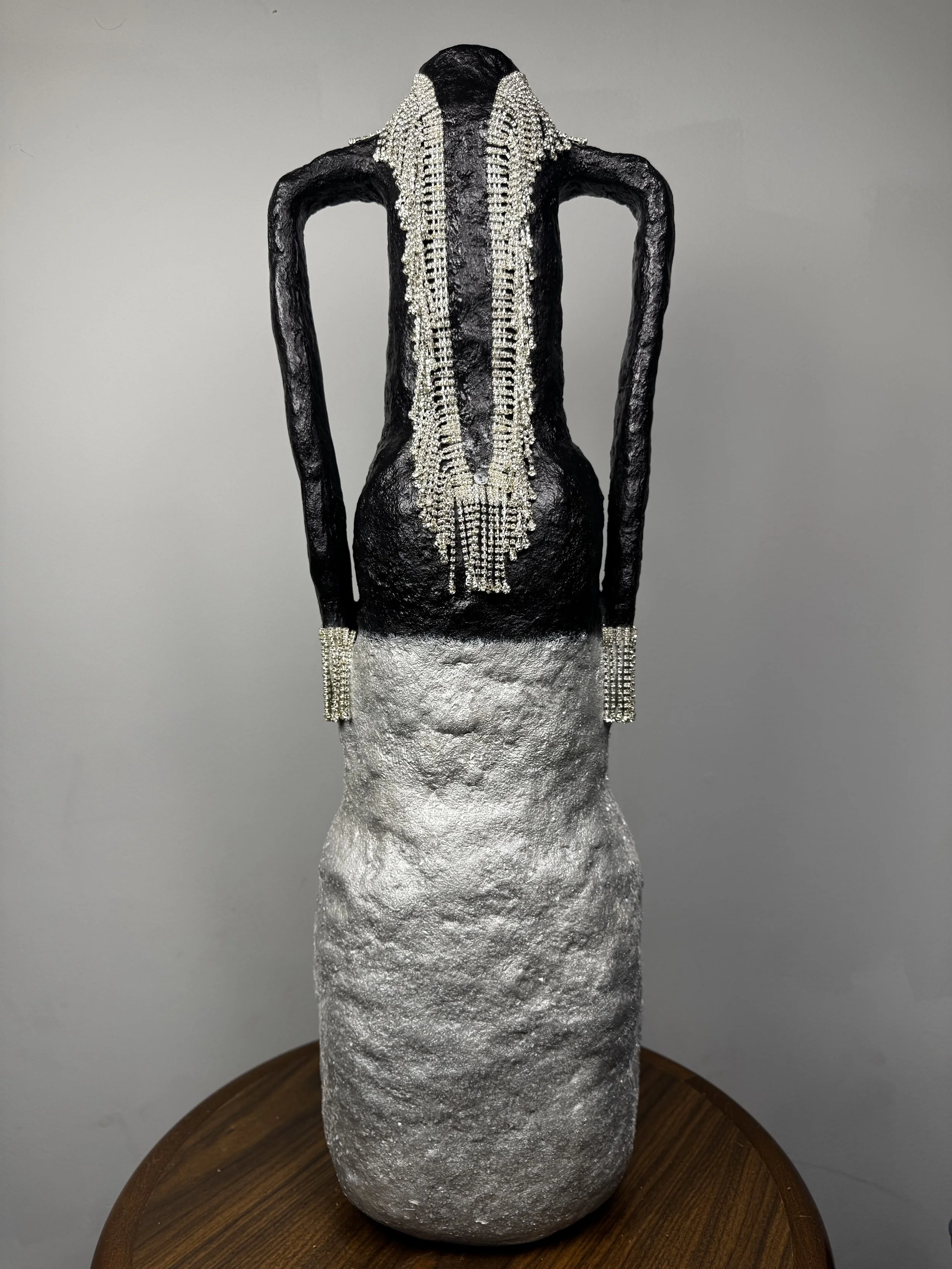 Title: Gala
•	Date: 2025
•	Medium: cement composite over recycled plastic, acrylic paint, baking soda, diamante trim
•	Dimensions: 28.5” x 7.5” x 7.5”
•	Description: Evoking the image of an evening gown with a full silver skirt, long black sleeves an