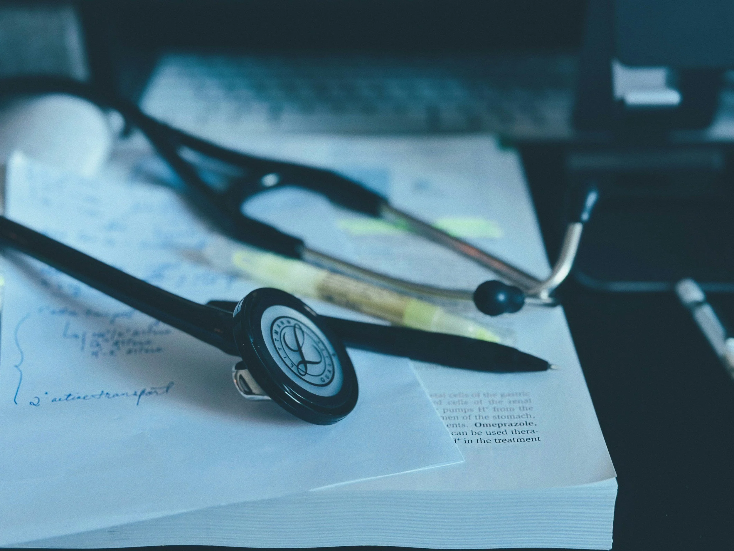 Stethoscope and pen resting on a pile of medical documents and notes on a desk.