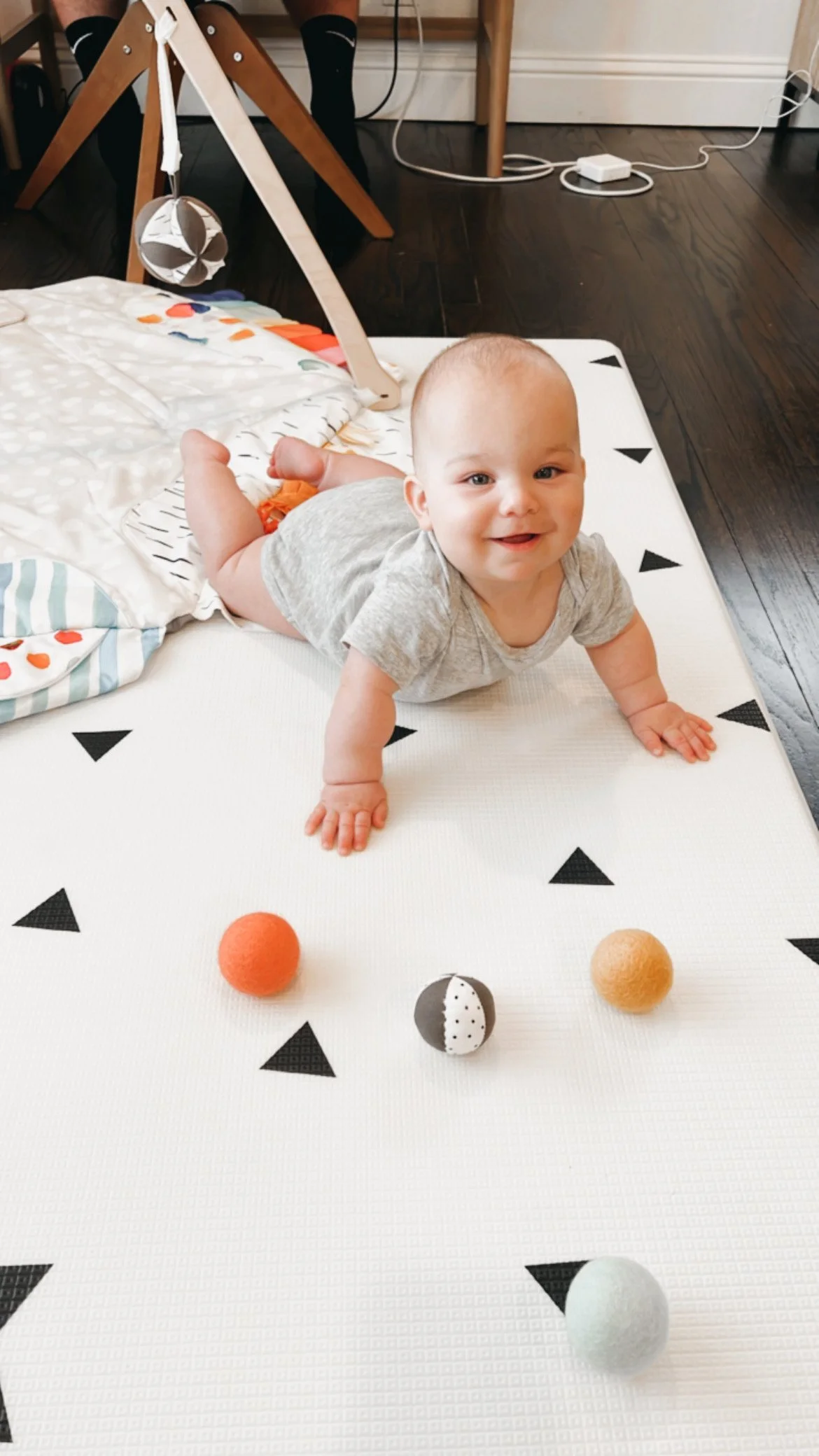 A young child with short hair, wearing a striped shirt, smiling and leaning over a couch in a playroom with toys in the background.
