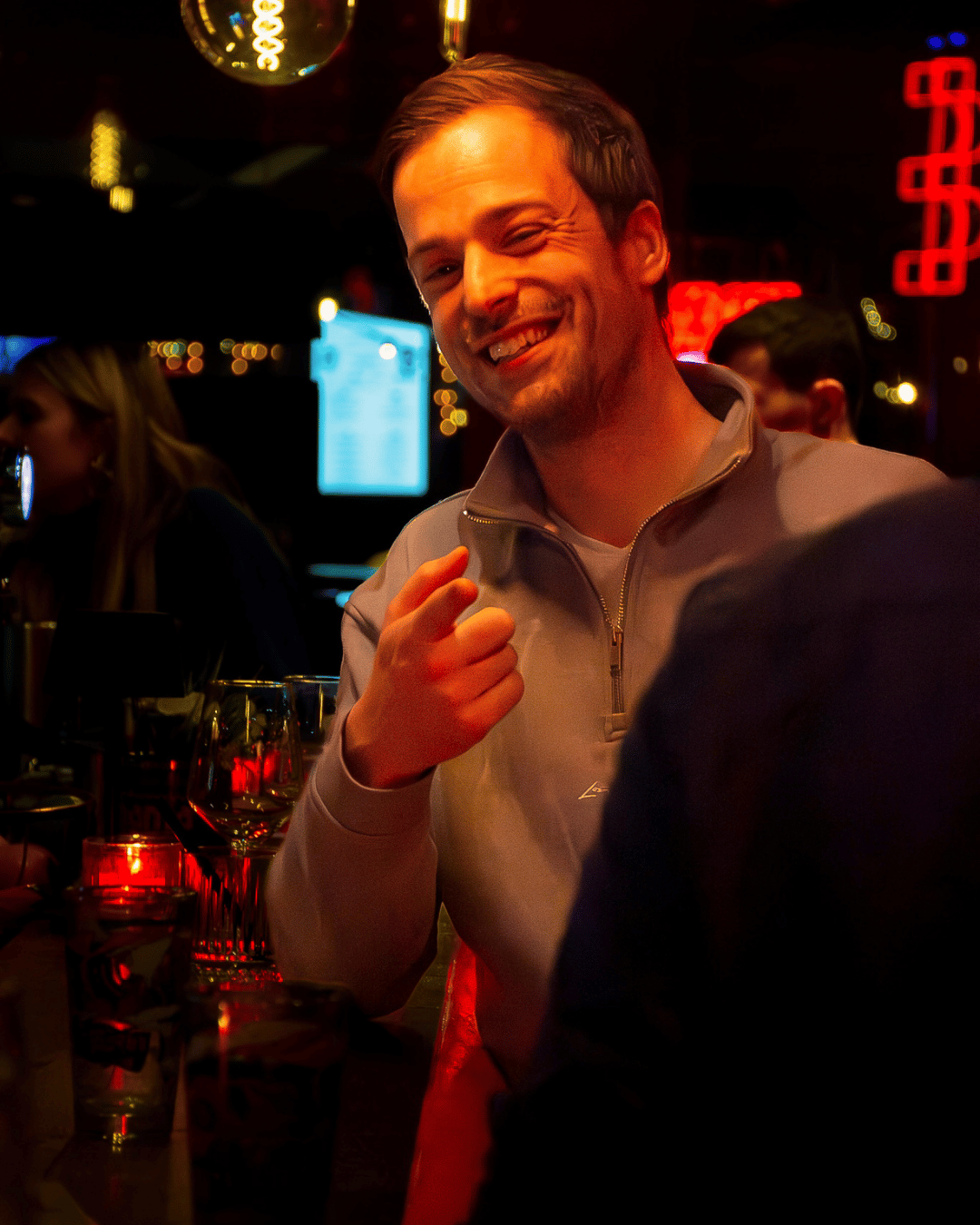 Man met een glimlach in een bar met kleurrijk neonverlichting.